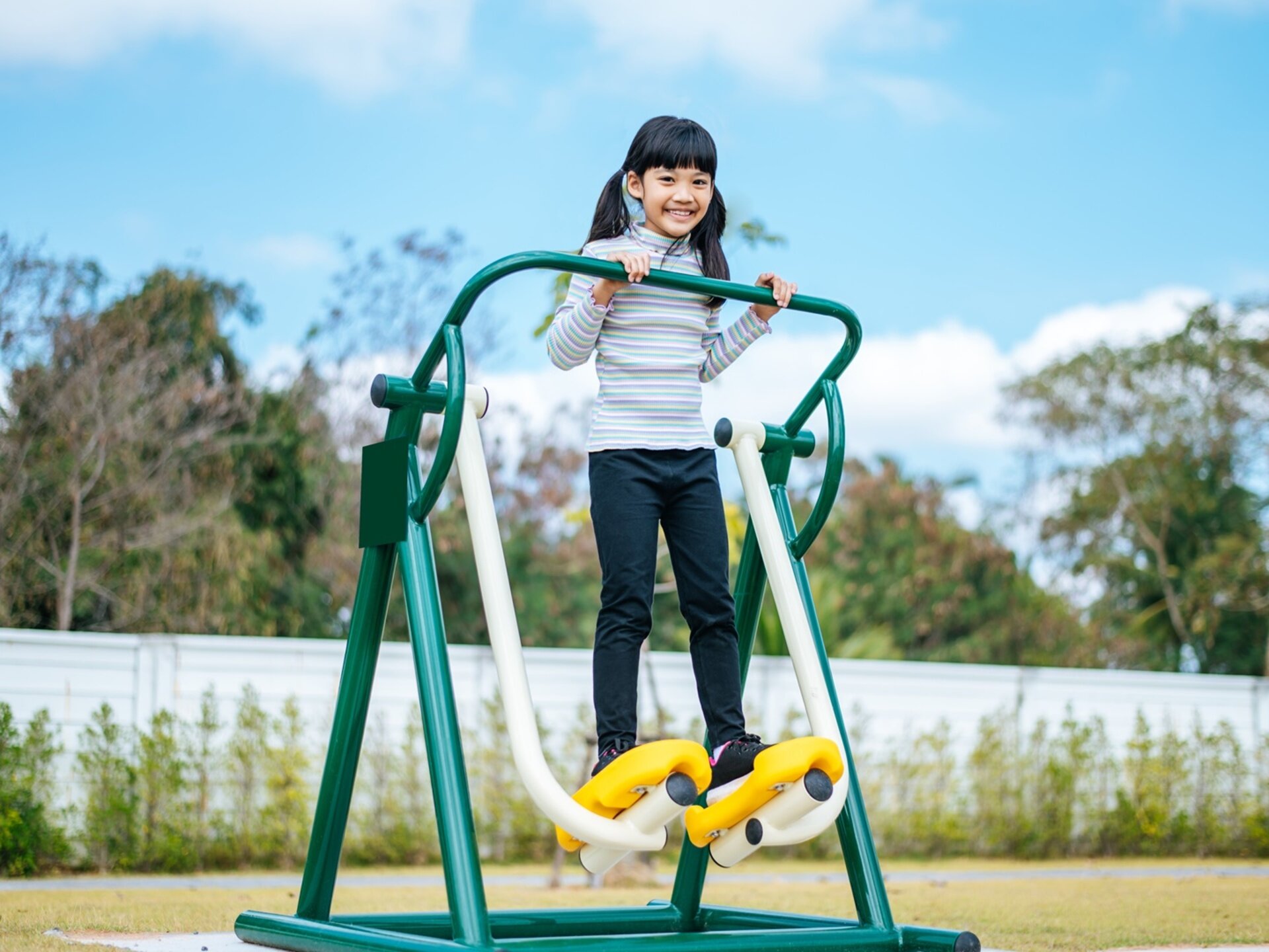 Zdjęcie przedstawiające dziewczynkę ćwiczącą na maszynie na zewnętrznej siłowni.