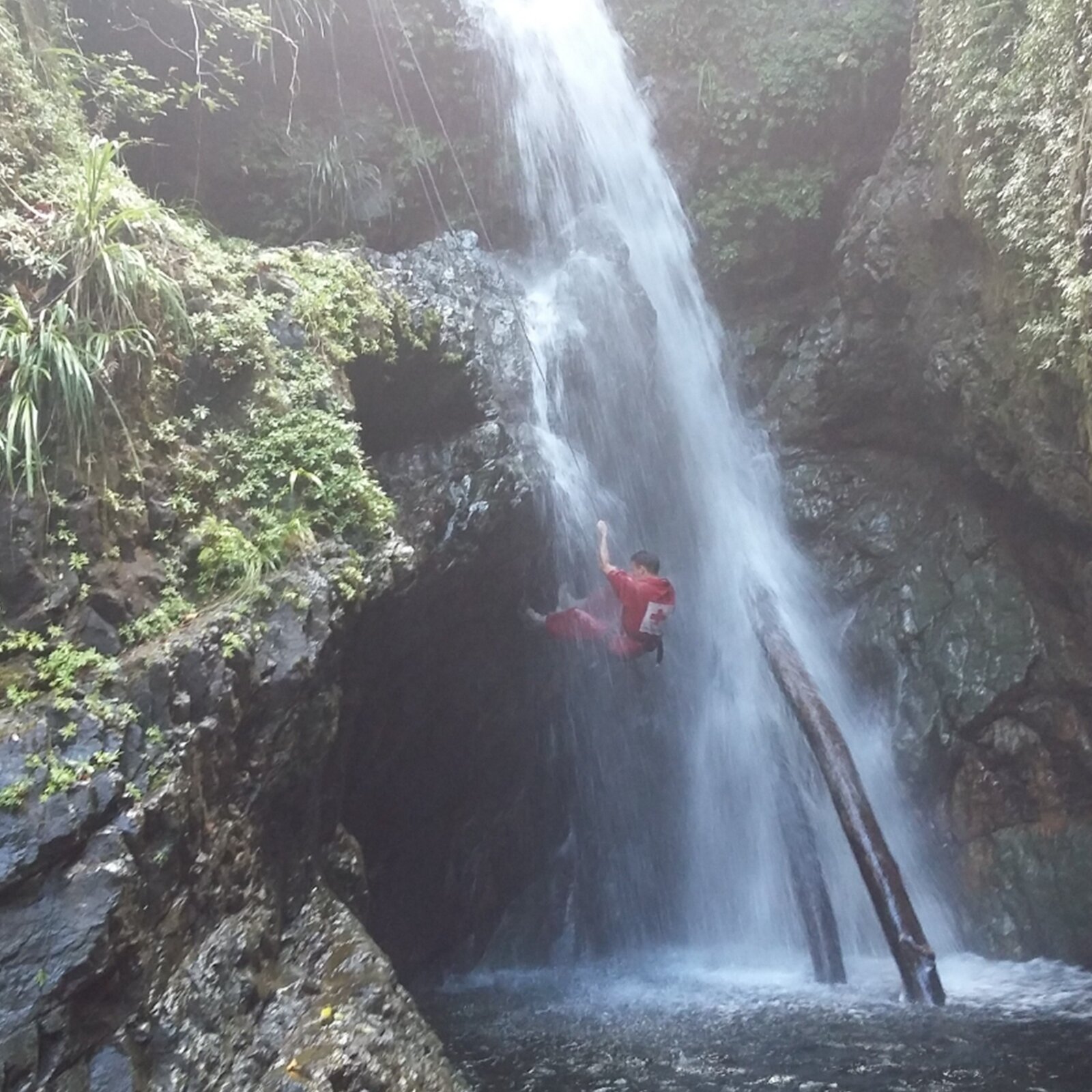 Ilustracja przedstawia mężczyznę zawieszonego na linie, który wspina się po stromej skale w środku wodospadu.