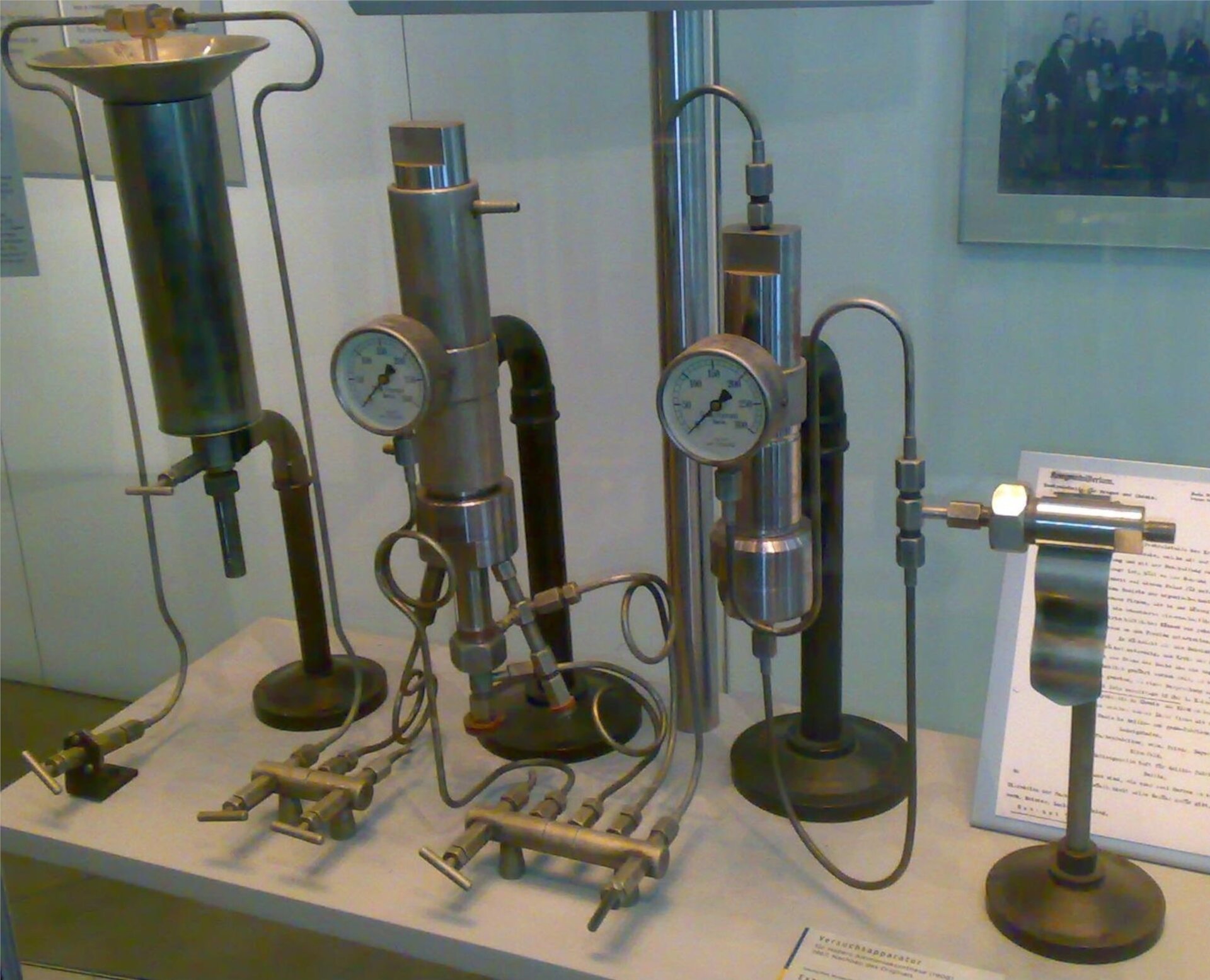 Zdjęcie przedstawia aparaturę. Na dwóch stojakach zamontowane są dwa metalowe walce. Są na nich okrągłe ciśnieniomierze, a w dolnej części zawory połączone przewodami z aparaturą.   
