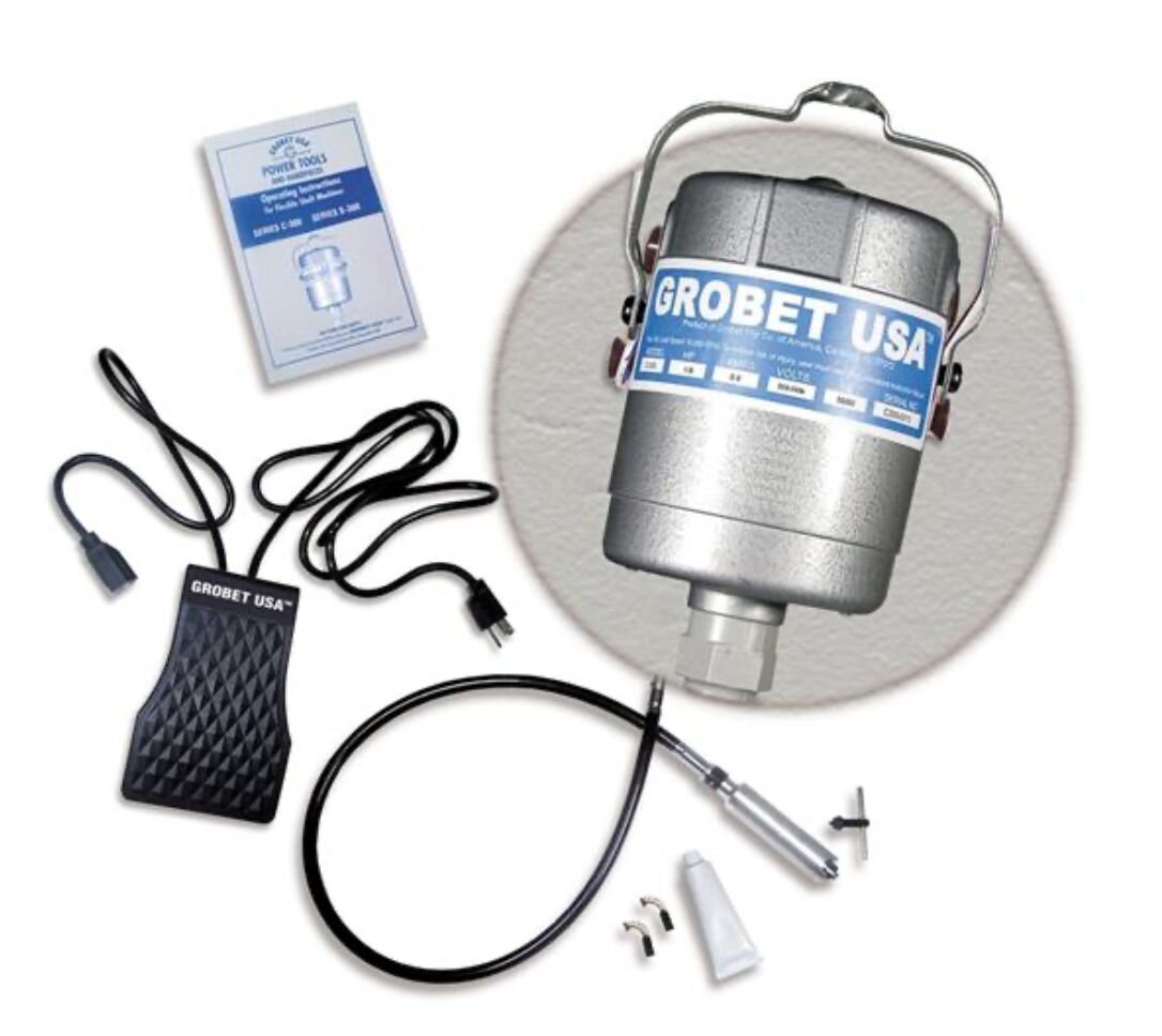 Zdjęcie przedstawia silnik w owalnej, stalowej obudowie z uchwytem. Silnik wyposażony jest w giętki wąż zakończony wałkiem. Obok niego leżą dwie końcówki do polerowania, tubka i niewielki wkrętak z motylkowym uchwytem. Obok silnika znajduje się także silikonowy pedał regulujący napęd, wyposażony w dwa przyłącza: do sieci i do silnika. 