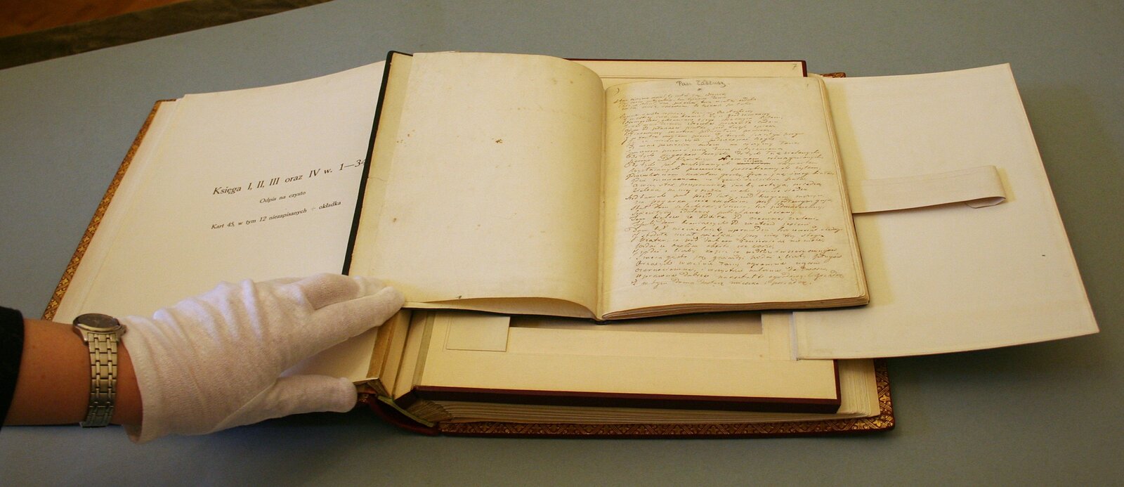 Zdjęcie przedstawia dwie otwarte księgi. Jedna leży na drugiej. Ta na wierzchu zapisana jest odręcznym pismem.