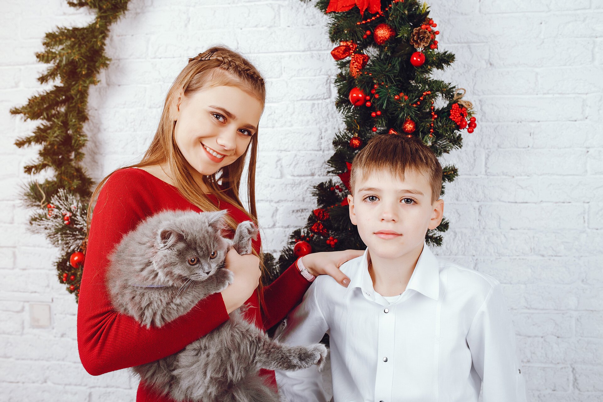 Zdjęcie przedstawia dwójkę dzieci od pasa w górę. Po lewo stoi uśmiechnięta nastolatka, która na prawej ręce trzyma kota, a jej lewa ręka położona jest na ramieniu stojącego obok młodszego chłopca. Dziewczyna ma na sobie czerwoną dopasowaną bluzkę, natomiast chłopiec białą koszulę. W tle za nimi ukazano duży wieniec świąteczny. 