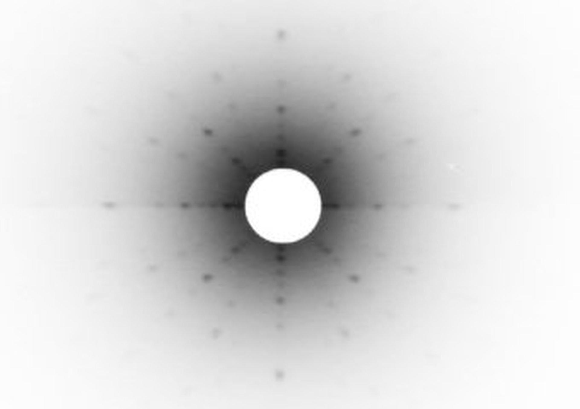 Rys. 6. Ilustracja przedstawia obraz dyfrakcji promieni X na krysztale o symetrii sześciennej. Czarne kropki to miejsca, w których nastąpiło interferencyjne wzmocnienie promieniowania X. Położenia tych kropek są zależne od długości użytego promieniowania i odzwierciedlają przestrzenną strukturę kryształu. Na samym środku ilustracji widoczne jest jasne koło. Od niego promieniście rozchodzą się szeregi ciemnych kropek. 