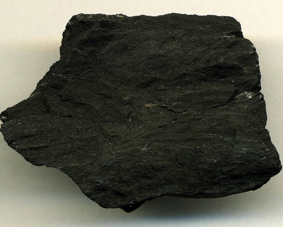 Na ilustracji przedstawiono węgiel kamienny. Skała ma nieregularny kształt, czarną barwę, nie posiada połysku.