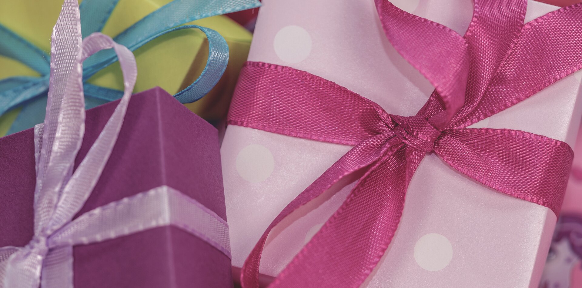 Zdjęcie trzech niewielkich paczuszek z prezentami. Każda zawinięta jest w ozdobny papier innego koloru i przewiązana kokardką. 