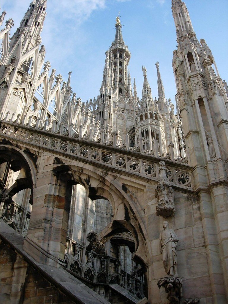 Zdjęcie ukazuje elementy katedry w Mediolanie, która jest perełką włoskiego gotyku. Są to części konstrukcji ozdobione ażurowymi ornamentami, sterczynami, płaskorzeźbami i rzeźbami.