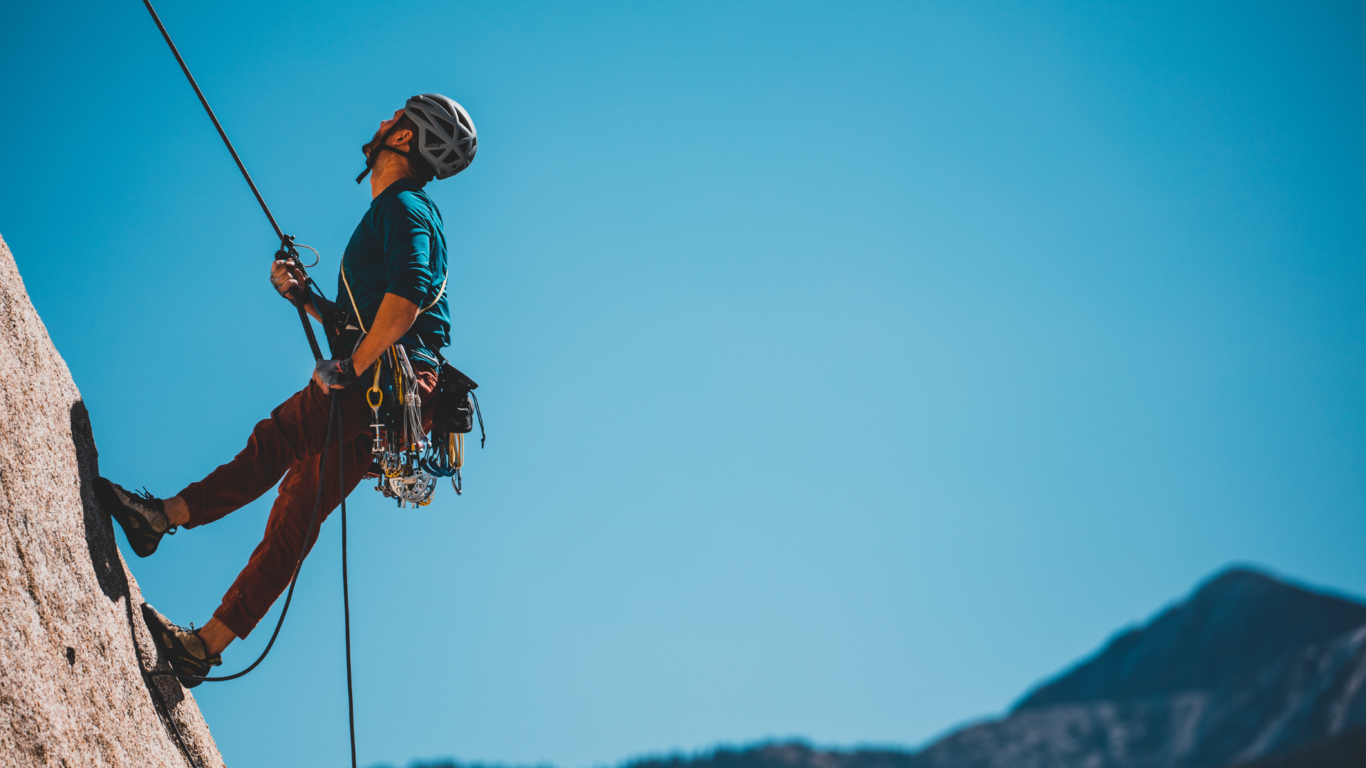 Zdjęcie przedstawia mężczyznę w kasku wspinającego się na linie na skałę.