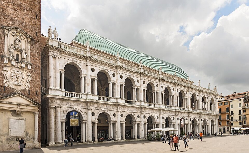 Zdjęcie przedstawia fragment renesansowej bazyliki na centralnym placu Vicenzy. Budynek ma dwie kondygnacje, na każdej znajduje się dziewięć arkad. Arkady oddzielają do siebie kolumny. Całość zwieńczona jest półokrągłym dachem.