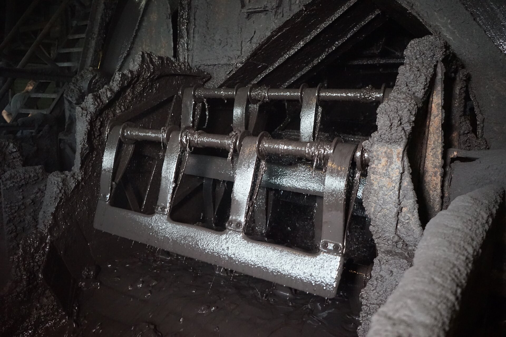 Zdjęcie przedstawia obrotowy wygarniacz łopatkowy wzbogacalnika zawiesinowego typu DISA. Wygarniacz stanowi usytuowany poziomo, równolegle do linii przelewu trzon, obracający się w trakcie pracy urządzenia wokół własnej osi. Wokół niego rozmieszczone są promieniście dookoła wspomnianej osi, na całej długości trzonu płaskie, prostokątne elementy, czyli łopatki. Element ten jest zamontowany tuż nad lustrem cieczy przed przelewem. Przyspiesza on wyodrębnianie koncentratu, zgarniając go z lustra cieczy za próg przelewowy koryta roboczego, czyli wyprowadza frakcję pływającą poza wzbogacalnik celem jej dalszej obróbki. Poniżej zdjęcia znajduje się przycisk multimedialny z nagraniem audio. Treść nagrania jest zgodna z tytułem zdjęcia.