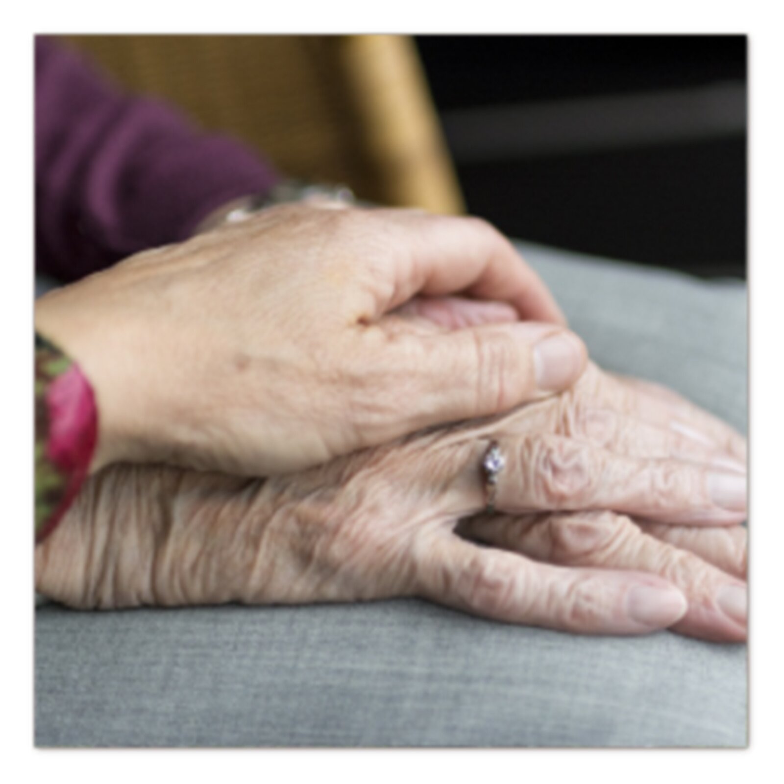 Zdjęcie przedstawia dłonie dwóch osób. Na ręce starszej kobiety kładzie dłoń młodsza osoba. 
