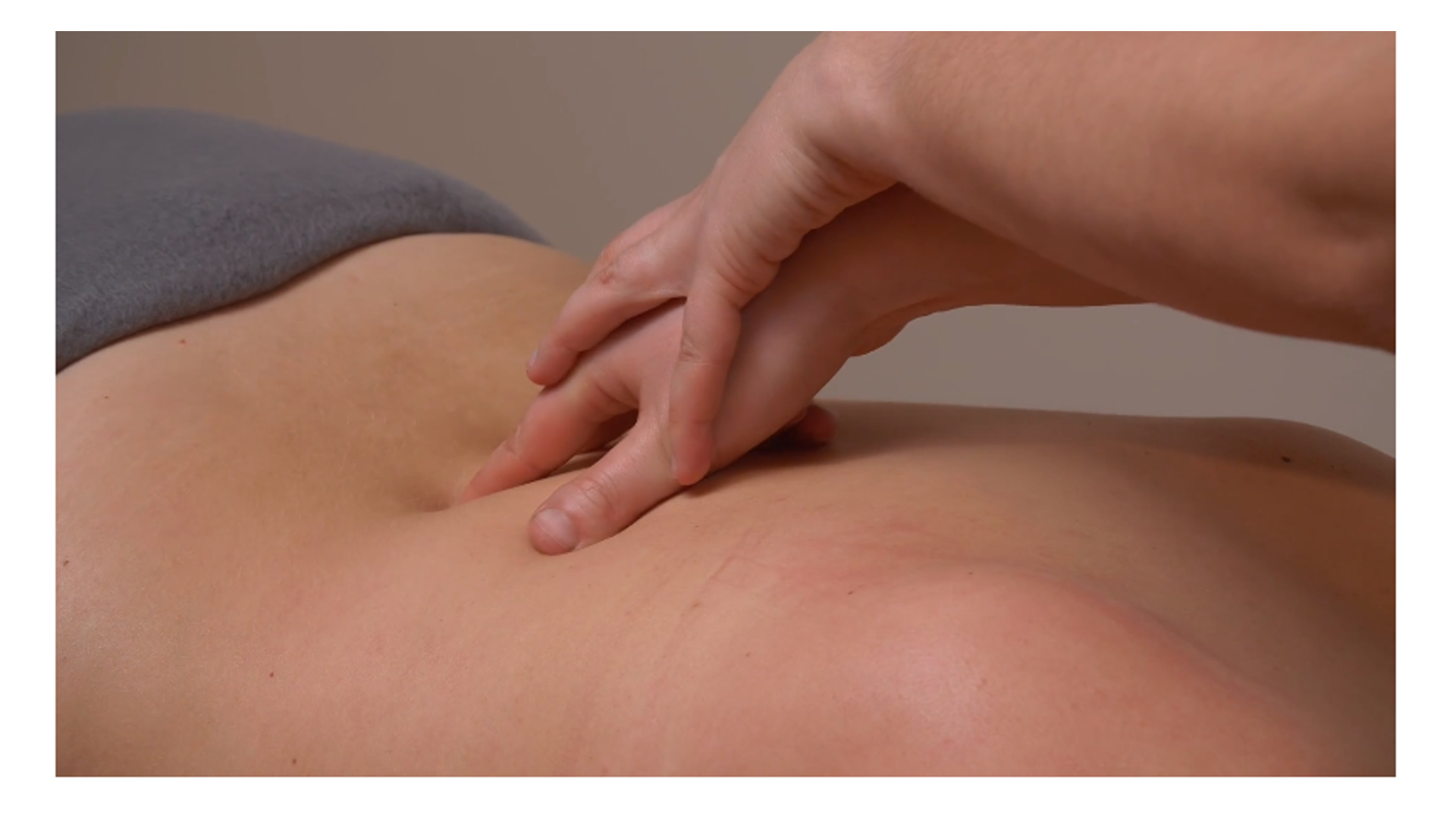 Zdjęcie pod tytułem uciski mięśni przykręgosłupowych. Zdjęcie przedstawia masażystkę, która wykonuje uciski dolnej części pleców pacjentki przy użyciu obu splecionych ze sobą rąk.