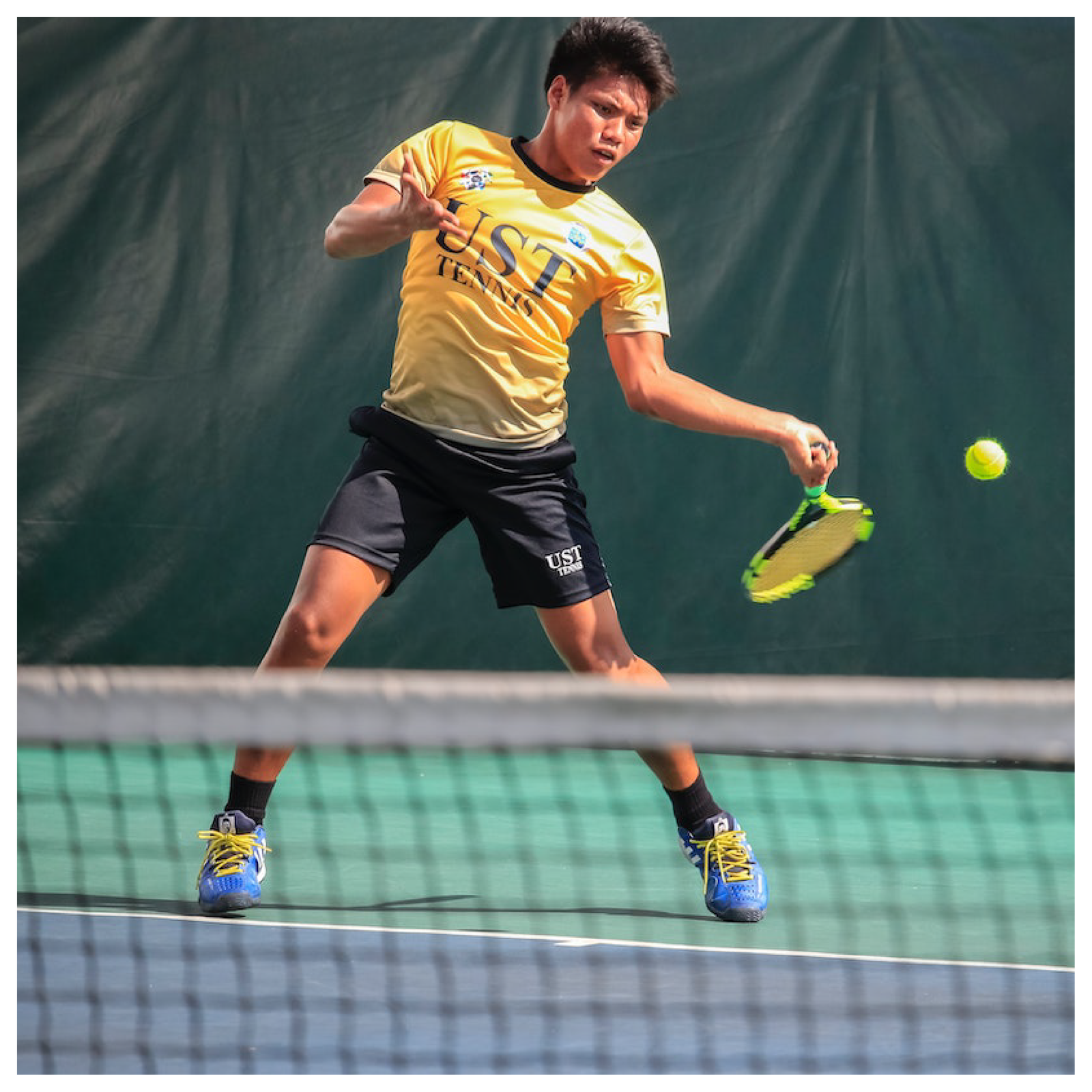 Obrazek przedstawia tenisistę na korcie który odbija piłkę. Na pierwszym planie siatka.