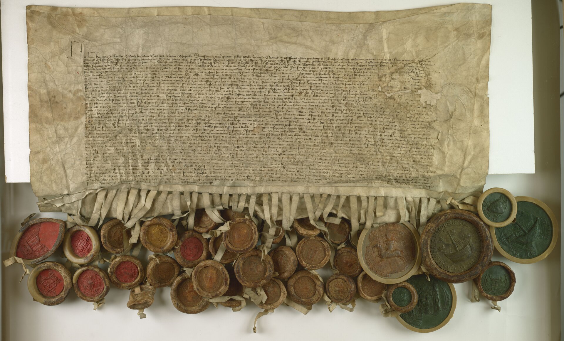 Na ilustracji stary dokument z nieczytelnymi napisami. Do niego są przywiązane liczne pieczątki, na dwóch widać łódź, a na jednej konia. 