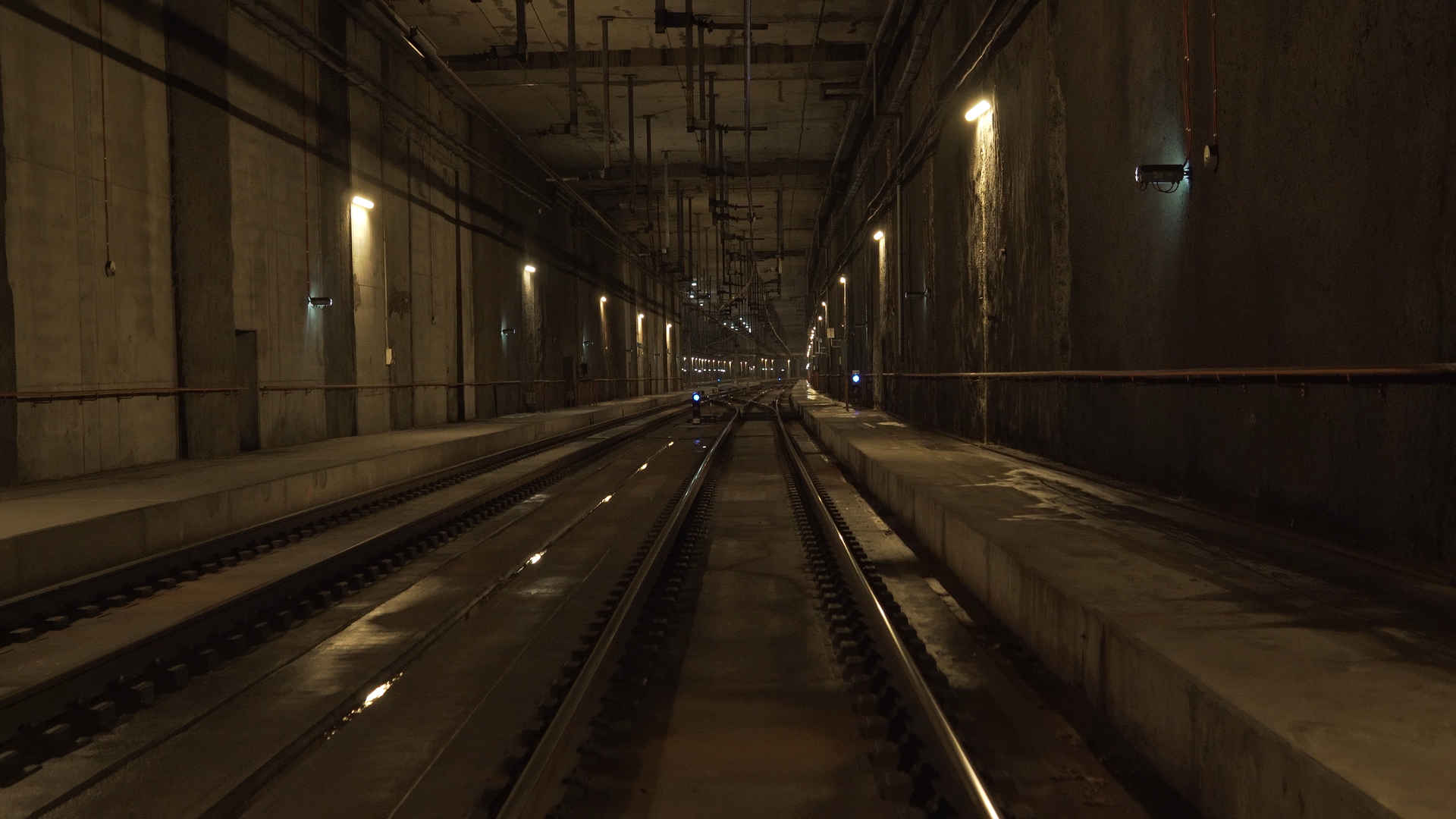 Ilustracja przedstawia tunel liniowy. Na zdjęciu widoczne są tory biegnące pod ziemią. Na ścianach znajdują się lampy. 