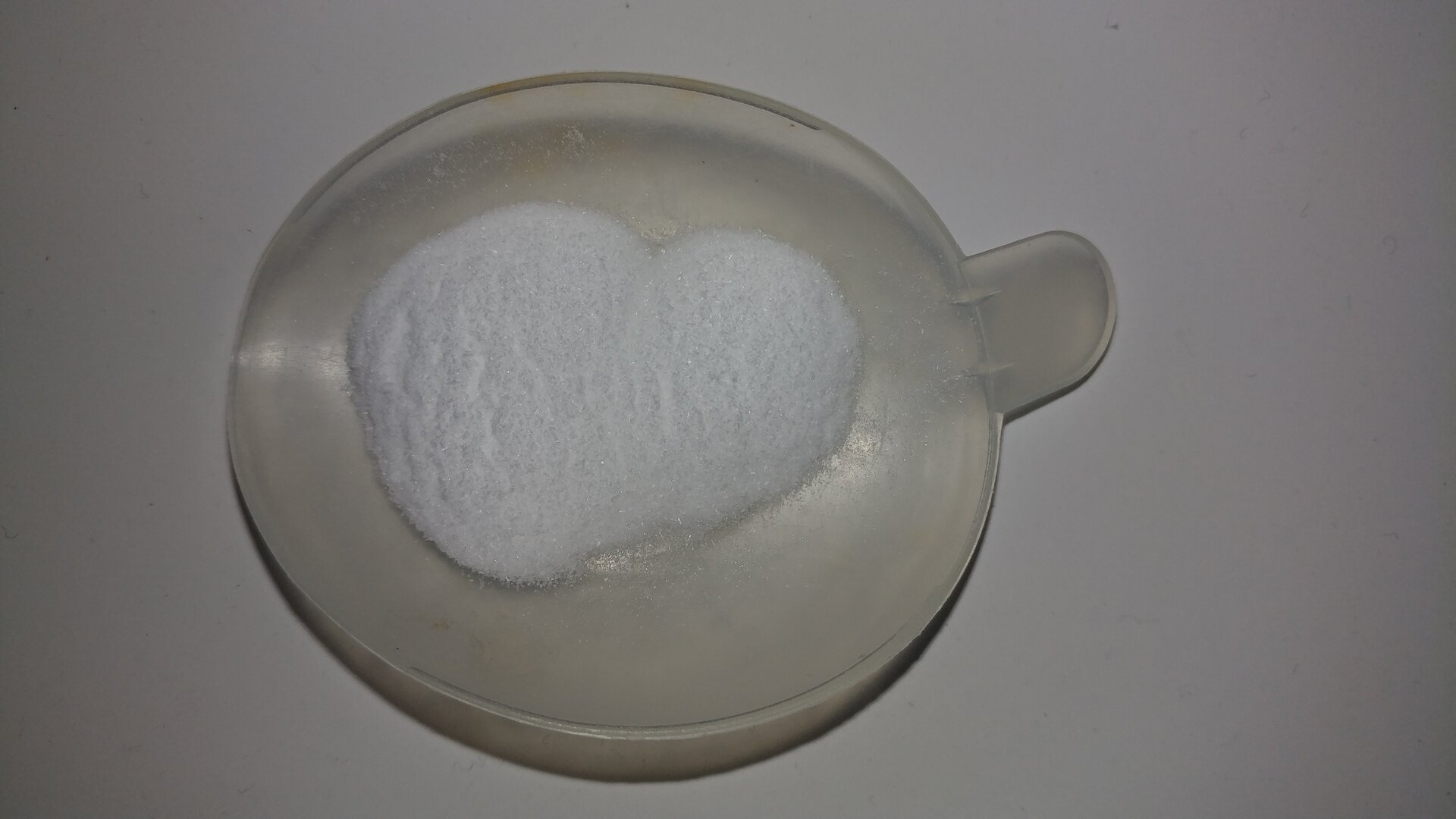 Grafika przedstawia białe drobnokrystaliczne ciało stałe na okrągłym naczynku. 