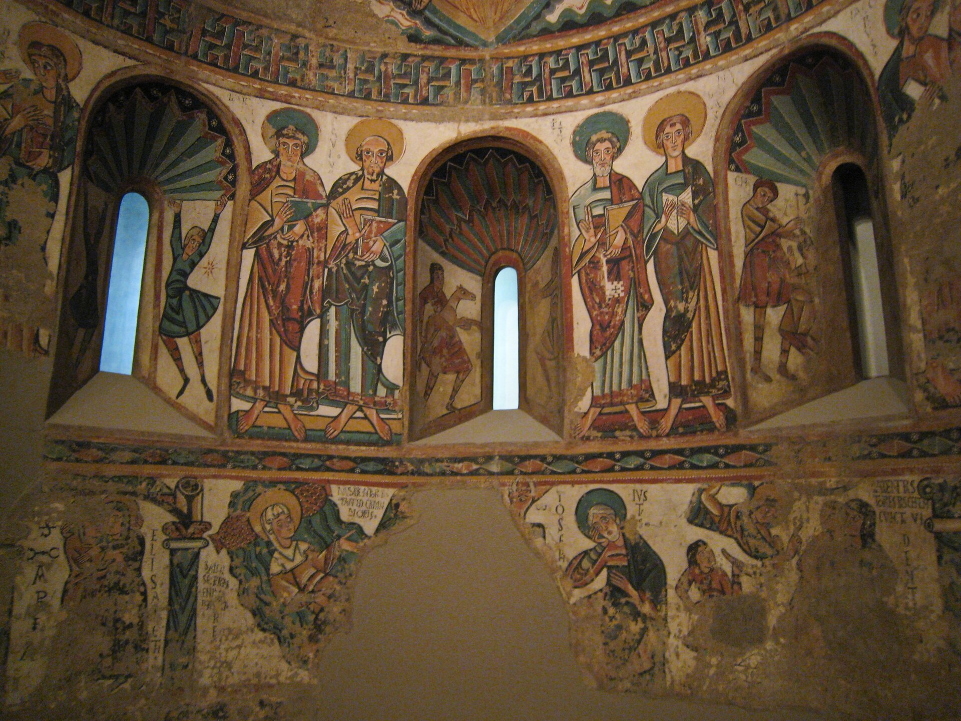 Ilustracja przedstawia malowidło „Chrystus Chwalebny i symbole czterech ewangelistów”. Na zdjęciu ukazane jest wnętrze z trzema małymi, podłużnymi oknami, zwieńczonymi łukami. Ściany pokryte są freskami o grubym, czarnym konturze, które skomponowane są w trzech pasach, oddzielonych ornamentami. Dolny, najgorzej zachowany pas z wieloma ubytkami, przedstawia sceny biblijne. Nad nim znajduje się pas z oknami, pomiędzy którymi umieszczone zostały w parach postacie świętych. Również wnęki okienne zostały pokryte malowidłami z postaciami i ornamentyką. Przedstawione freski odznaczają się niezwykle bogatą kolorystyką. Dominującymi barwami są: biel, ciepła żółć, czerwień i błękit. 