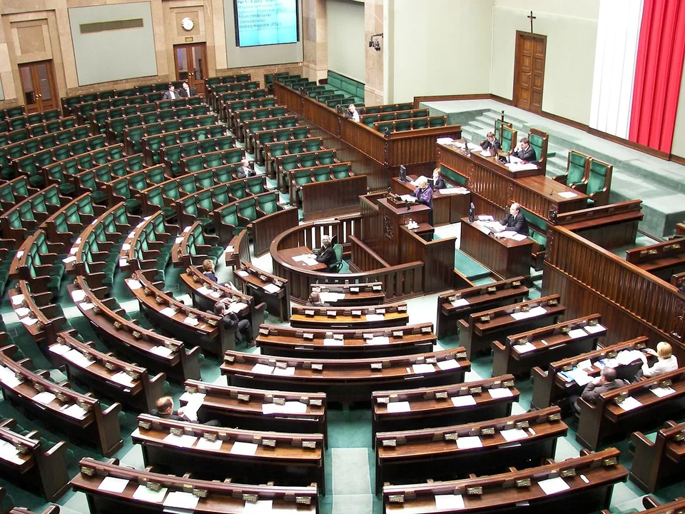 Sejm RP - sala plenarna. Sala sejmowa - duża, półkolista. W centralnej części znajduje się podwyższona mównica. Wokół niej, w układzie półkola, rozmieszczone są kolejne rzędy siedzeń dla posłów na stopniowanych poziomach.