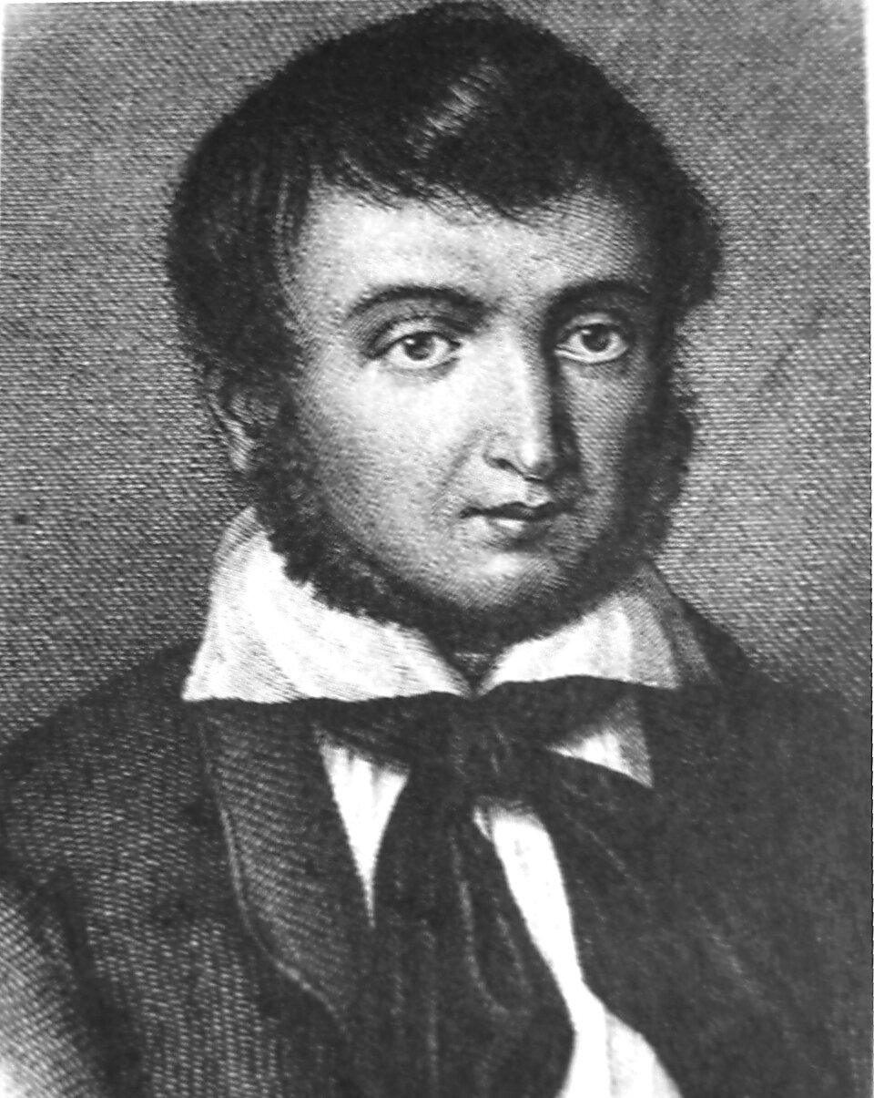 Ilustracja przedstawia portret mężczyzny w sile wieku. Postać ukazana jest od piersi w górę. Mężczyzna prezentuje prawy półprofil. Jego twarz jest okrągła. Mężczyzna ma dość wysokie, gładkie czoło. Włosy mężczyzny są krótkie, proste. Grzywka sięgająca połowy czoła jest zaczesana na lewą stronę. Ma wąskie, ciemne brwi. Oczy postaci są duże. Nos mężczyzny jest długi, lekko zgarbiony. Jego usta są małe. Mężczyzna ma wąskie bokobrody i zarost na brodzie. Jest ubrany w koszulę z wysokim kołnierzem i wysoko zapiętą marynarkę. Na szyi ma zawiązaną apaszkę.