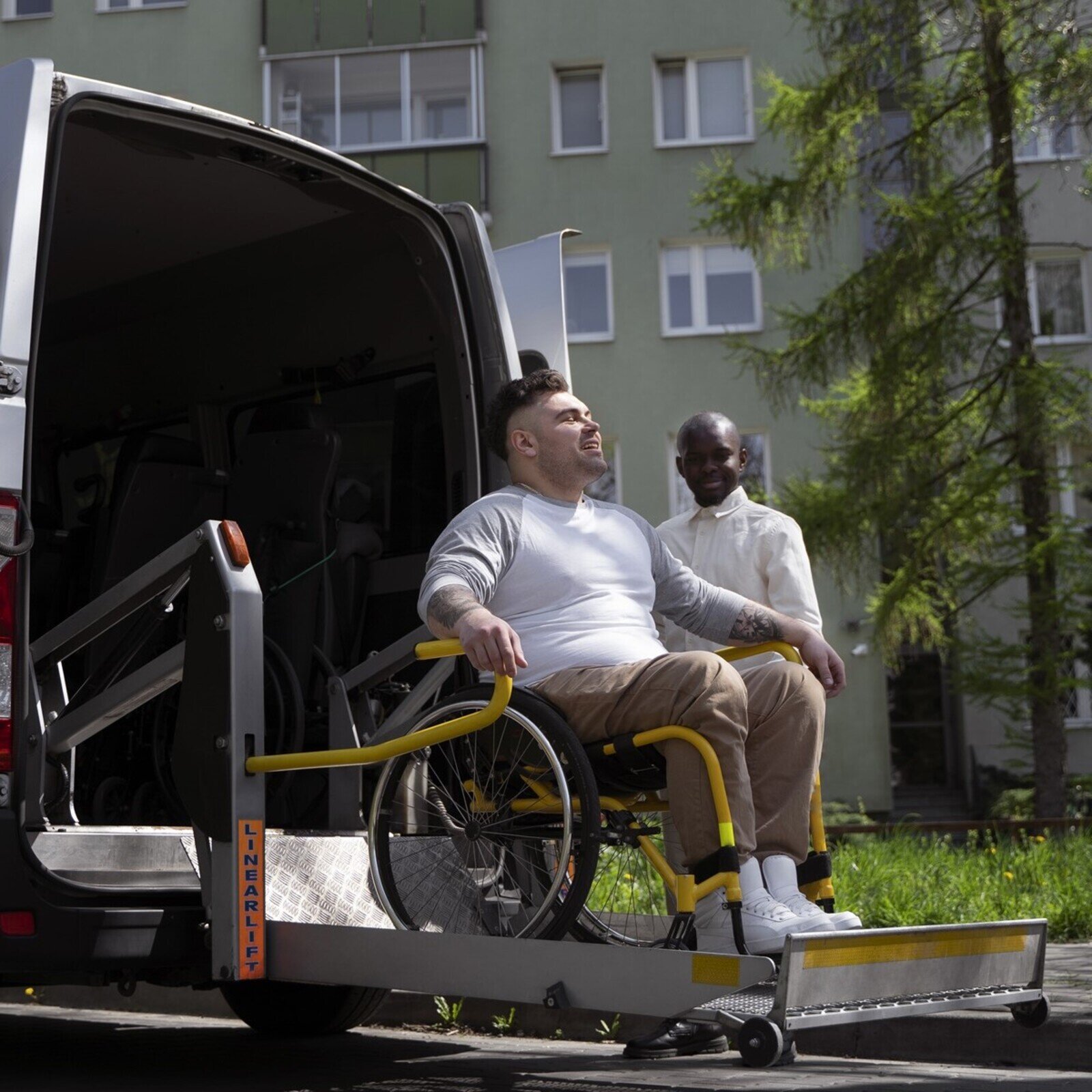 Zdjęcie przedstawia osobę na wózku inwalidzkim zjeżdżającą na platformie z samochodu.