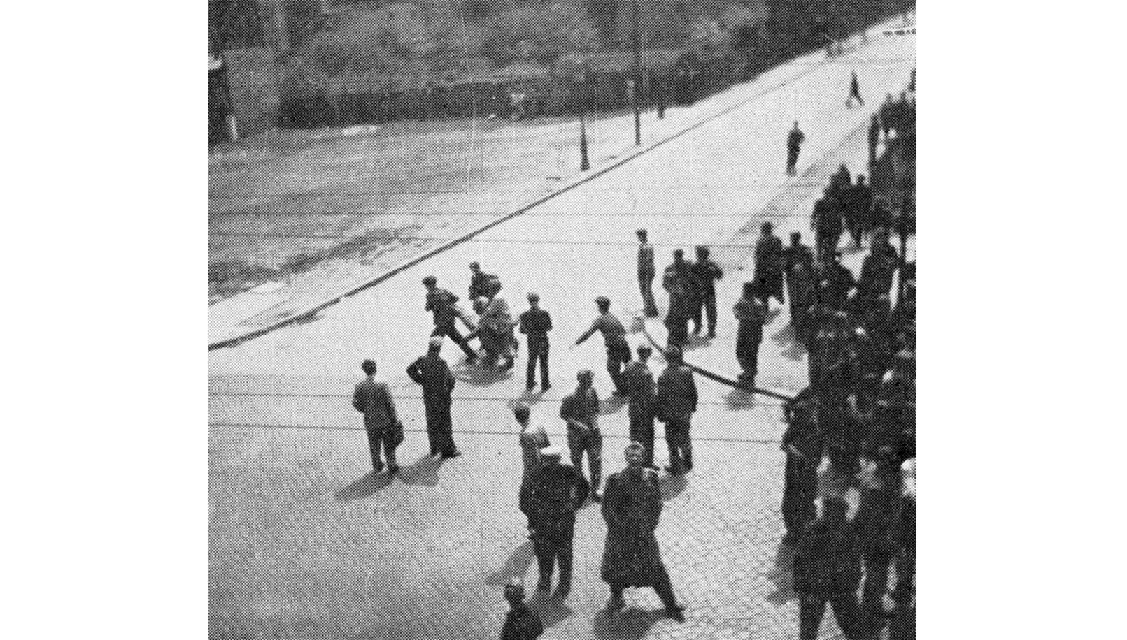 Czarno-biała fotografia przedstawiająca demonstrantów na skrzyżowaniu ulic. Kilku z nich niesie rannego (1956 r.)