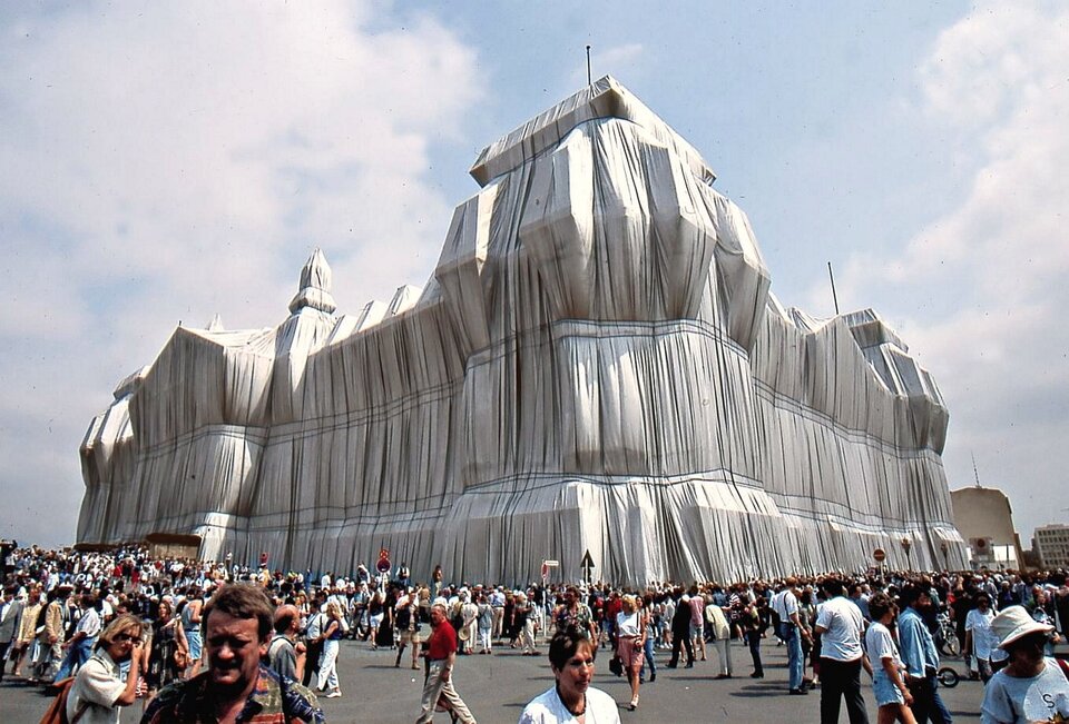 Ilustracja przedstawia dzieło Christo i Jeanne‑Claude pt. „Wrapped Reichstag (Opakowany Reichstag)”. Na zdjęciu widoczny jest opakowany płachtami srebrnego, ognioodpornego materiału niemiecki parlament. Instalacji przyglądają się tłumy gapiów.