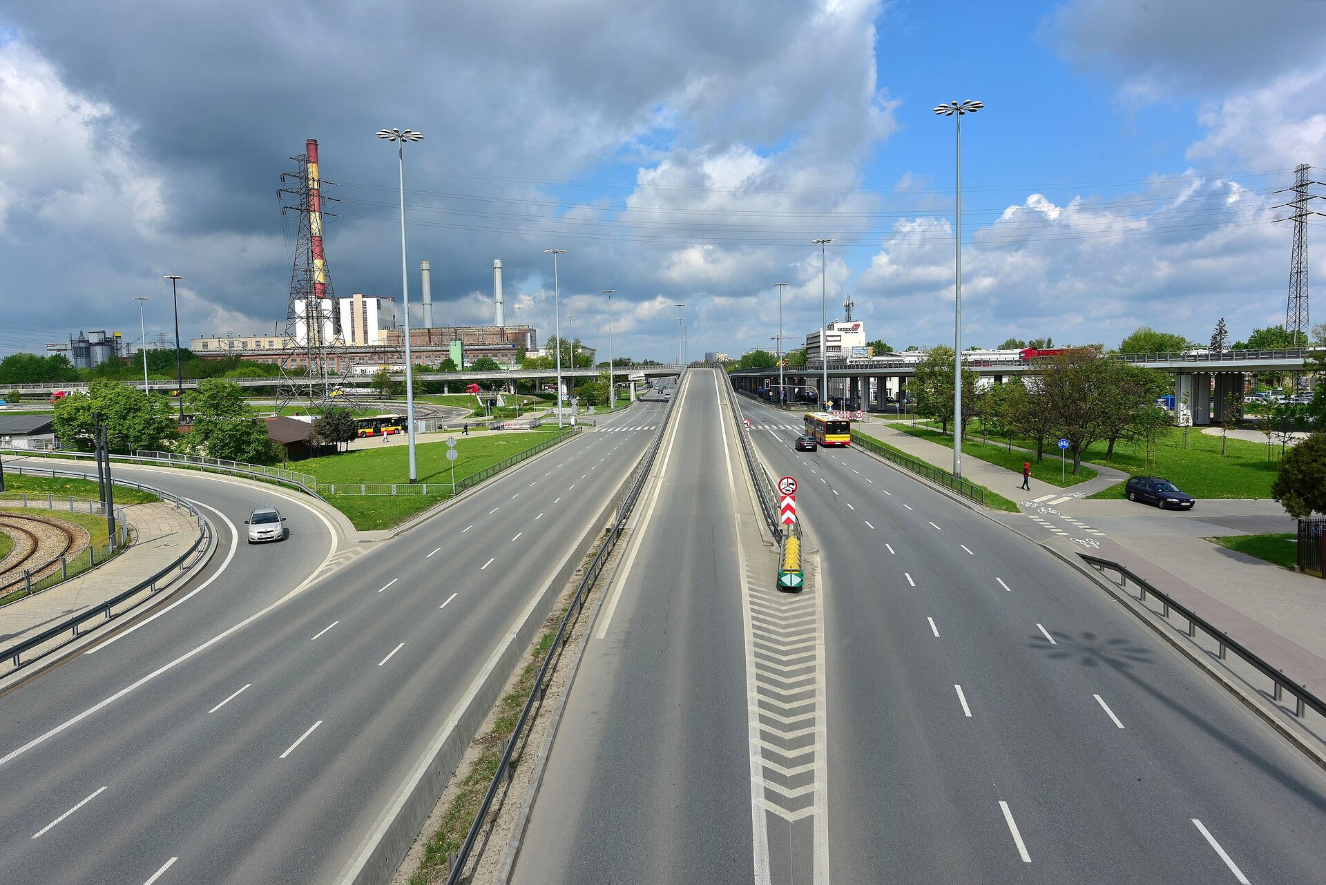 Na zdjęciu szeroka, trzypasmowa ulica o nazwie Trasa Toruńska, na dalszym planie elektrociepłownia Żerań.