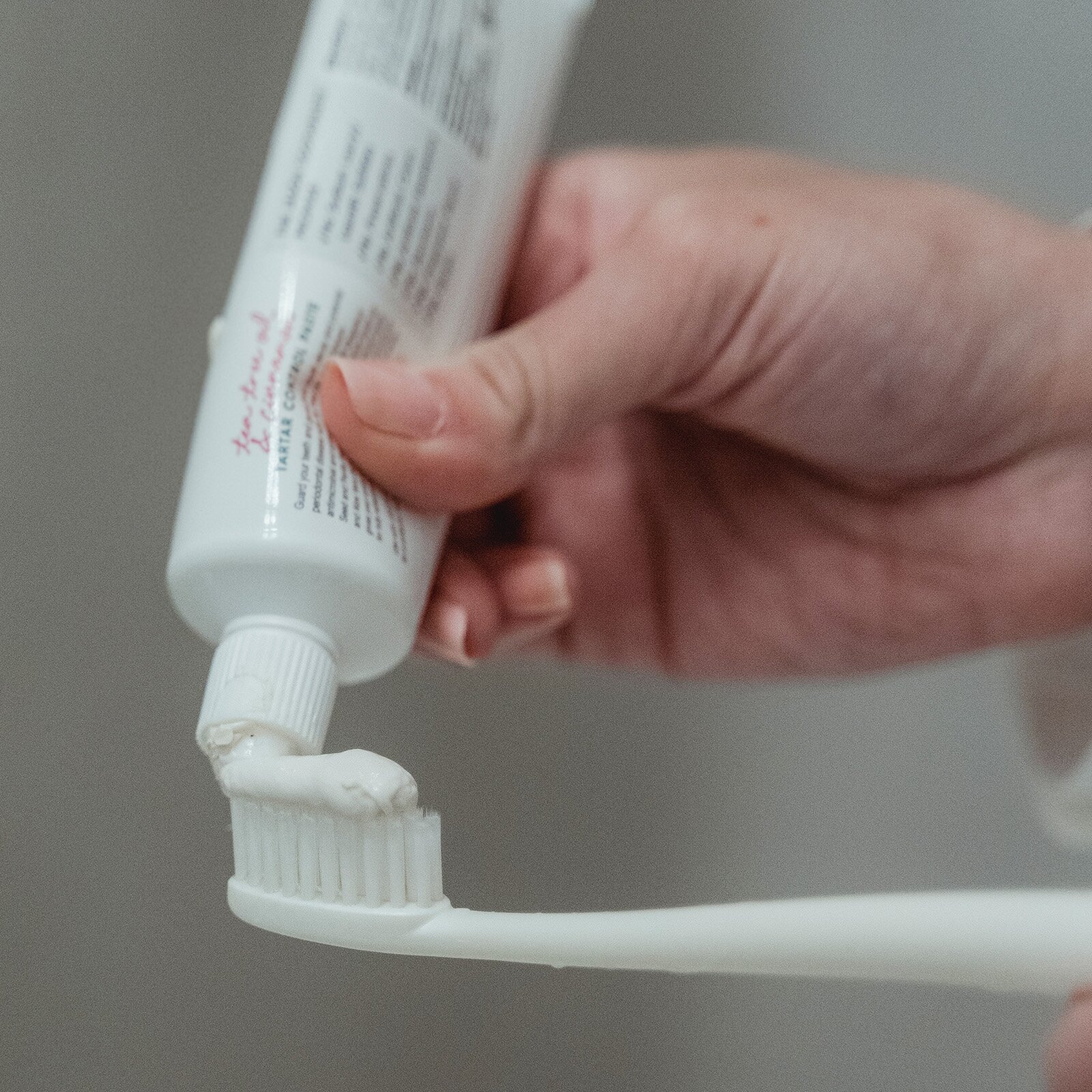 Zdjęcie przedstawia osobę, która wyciska pastę do zębów z tubki na szczoteczkę.