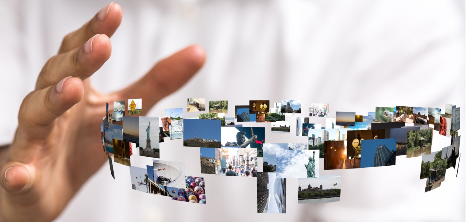 Grafika komputerowa przedstawia obraz nierzeczywisty. Duża ręka człowieka, znajdująca się z lewej strony zbliża się do małych fotografii ułożonych w okręgu. Fotografii jest bardzo dużo, nie wszystkie są dobrze widoczne. Wyglądają tak, jakby wirowały w powietrzu. Na fotografiach znajdują się ulice miast, fragmenty parków, wysokich bloków, zwierzęta, pomniki, ludzie, niebo, znaki drogowe, zachody słońca, las, łąka, zabawki. 