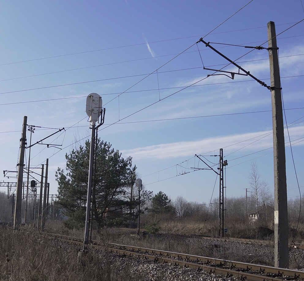 Zdjęcie przedstawia sekcję, czyli odcinek naprężenia. Na zdjęciu widać odcinek toru kolejowego. Przy torze stoją słupy sieci trakcyjnej oraz semafory. W tle widać drugi tor i drzewo między torami.