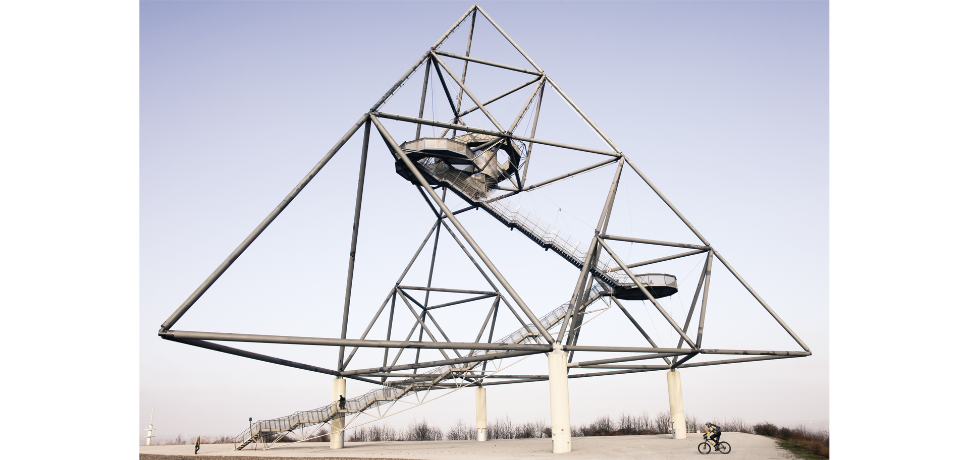 Zdjęcie przedstawia stalową konstrukcję w kształcie ostrosłupa o trójkątnej postawie, wewnątrz której znajdują się schody.