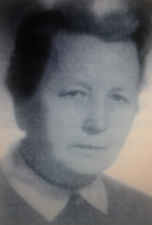 Kliknij, aby powiększyć Zdjęcie słabej jakości. Starsza kobieta z spiętym włosami. Ubrana jest w sweter na którym wyłożony jest kołnierzyk.