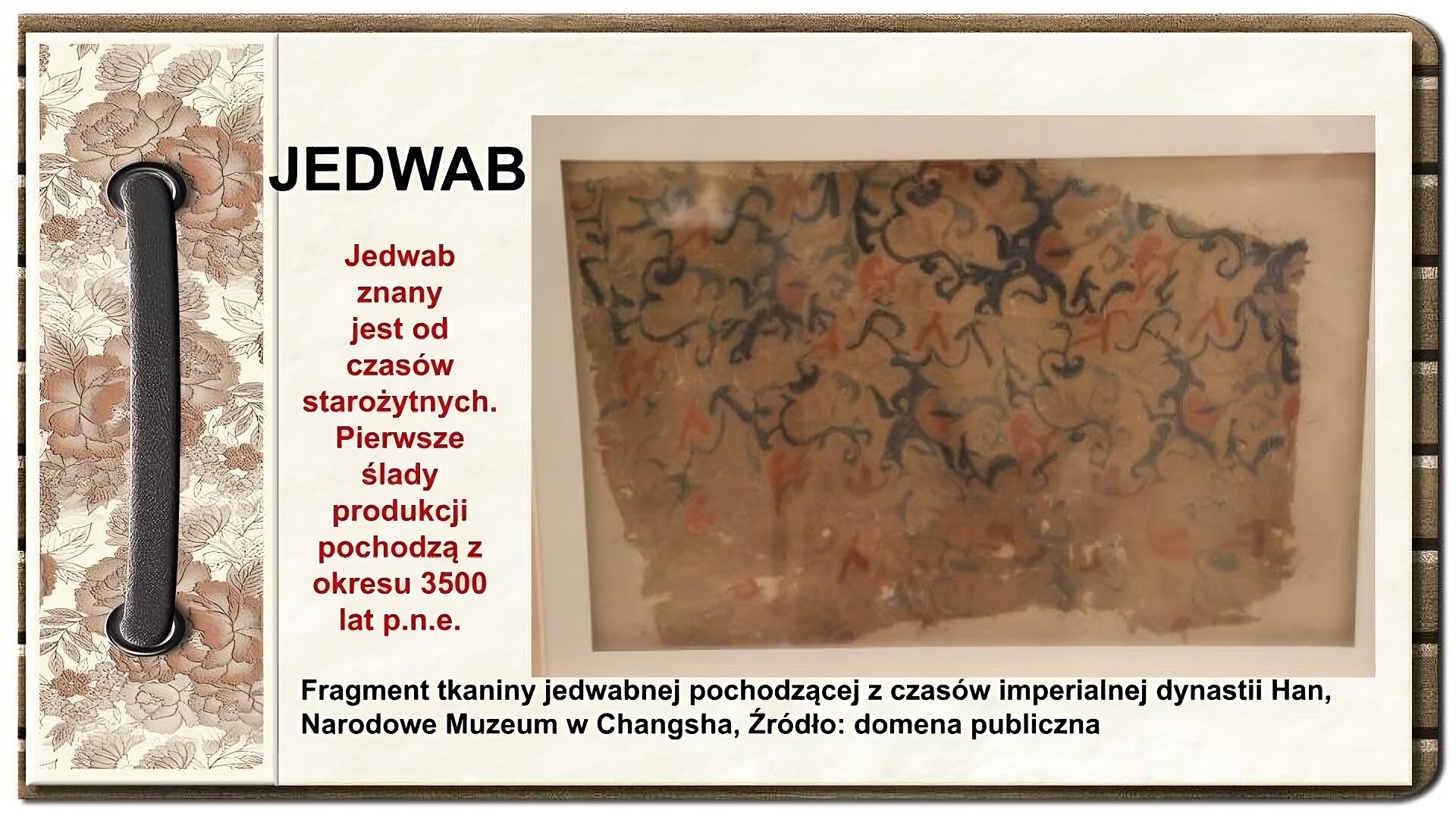 Slajd zatytułowany „Jedwab”. Tekst na slajdzie: Jedwab znany jest od czasów starożytnych. Pierwsze ślady produkcji pochodzą z okresu 3500 lat p.n.e. Po prawej stronie ilustracja przedstawia oprawiony płat skrawka jedwabiu z czasów starożytnych Chin. Tkanina, zawiera nieregularne okrężne i podłużne motywy geometryczne w odcieniach czerni i czerwieni. Dolny płat tkaniny poszarpany, zawierający ślady użytkowania. Całość zachowanego zabytku znajduje się za oprawą szklaną w ramie obrazu. Po lewej stronie ornament zdobiący slajd w formie motywów roślinnych, na których nałożono stylizowaną, metalową obwódkę spinającą stronę.