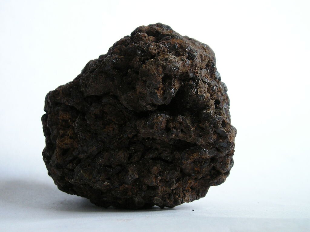 Na zdjęciu widoczna jest bryła torfu. Ma ona ciemny kolor i obły kształt. Torf ma porowatą strukturę.