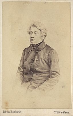 Zdjęcie przedstawia mężczyznę w średnim wieku. Mężczyzna ma poważny wyraz twarzy. Jego włosy są gęste, zaczesane do góry. Mężczyzna jest ubrany w surdut.  