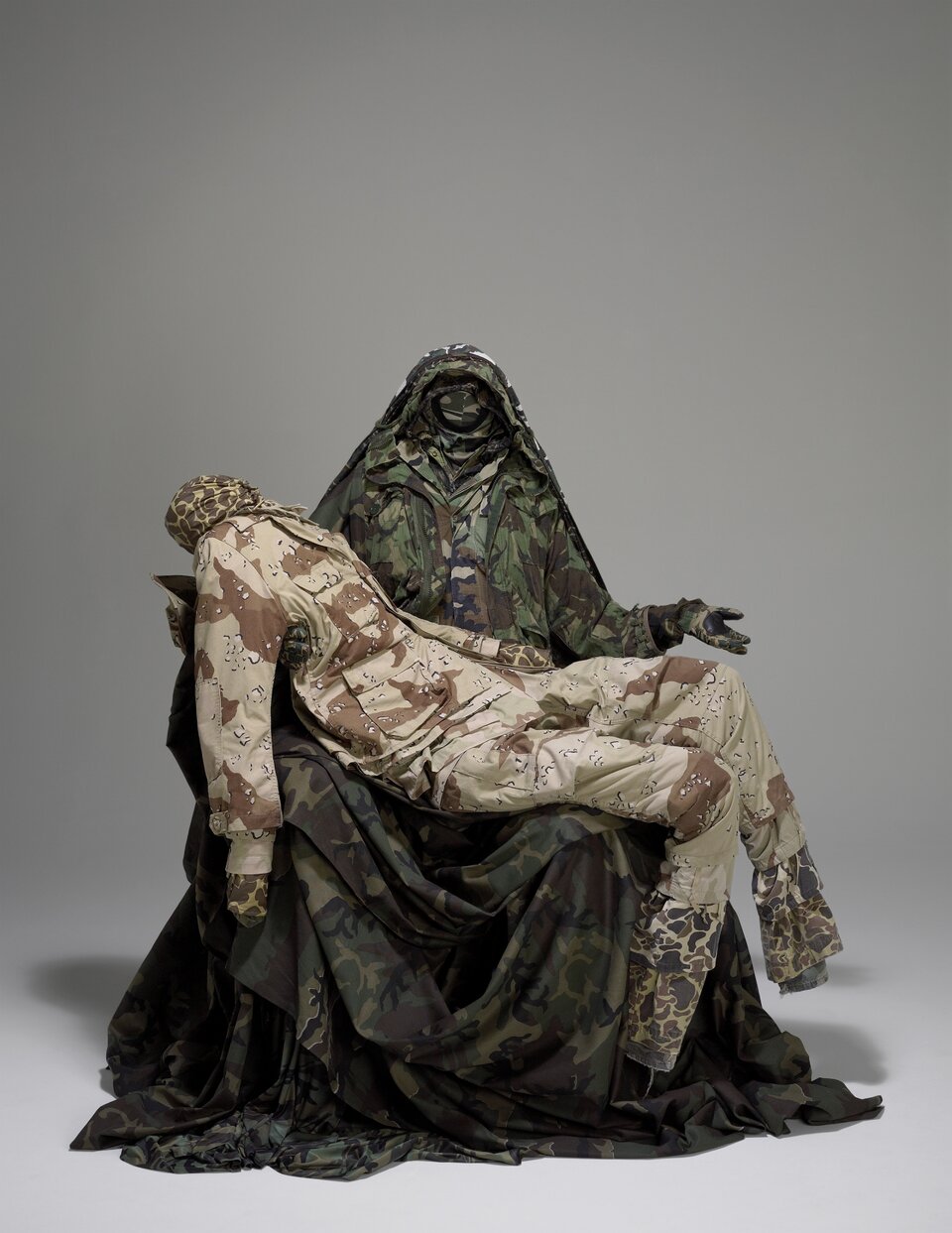 Instalacja pod tytułem "Pieta", autorstwa Guerra de la Paza, przedstawia dwie postacie bez twarzy w wojskowych ubraniach. Jedna postać siedzi i trzyma w swoich ramionach leżącą postać. 