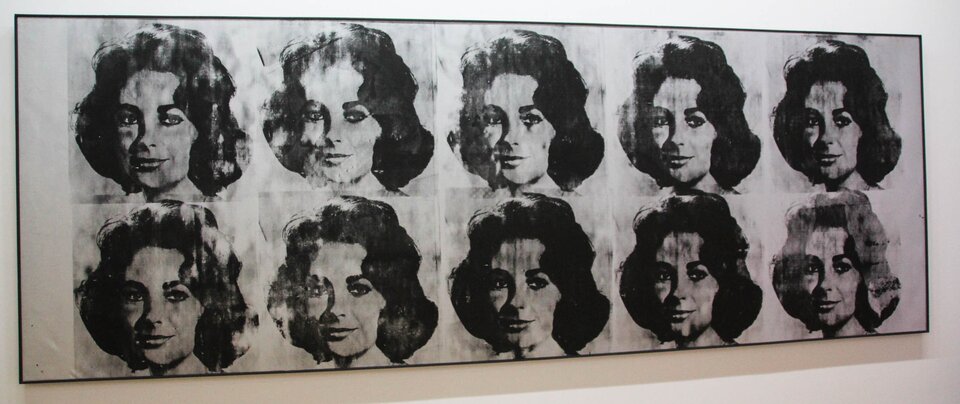 Ilustracja przedstawia dzieło Andy'ego Warhola „Ten Lizes”. Ukazuje zwielokrotniony portret Elizabeth Tylor o falowanych włosach, które sięgają do ramion. Wizerunki rozmieszczone są w dwóch rzędach po pięć twarzy w każdym. Grafika jest czarno‑biała. Poszczególne portrety różnią się stopniem nasycenia i jakością odbicia. 