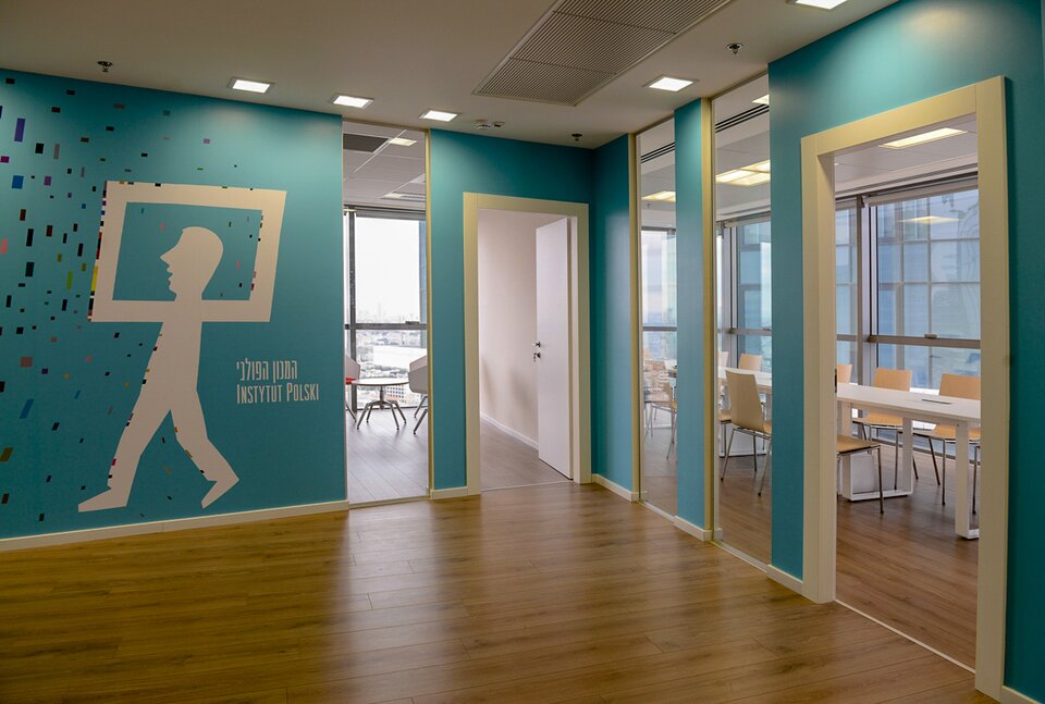 Zdjęcie przedstawia wnętrze sali. Jest ona pusta. Widoczne są dwie pary drzwi, które prowadzą do innych pomieszczeń. Na jednej ze ścian widać namalowaną postać człowieka, którego głowa znajduje się w prostokątnej ramie.