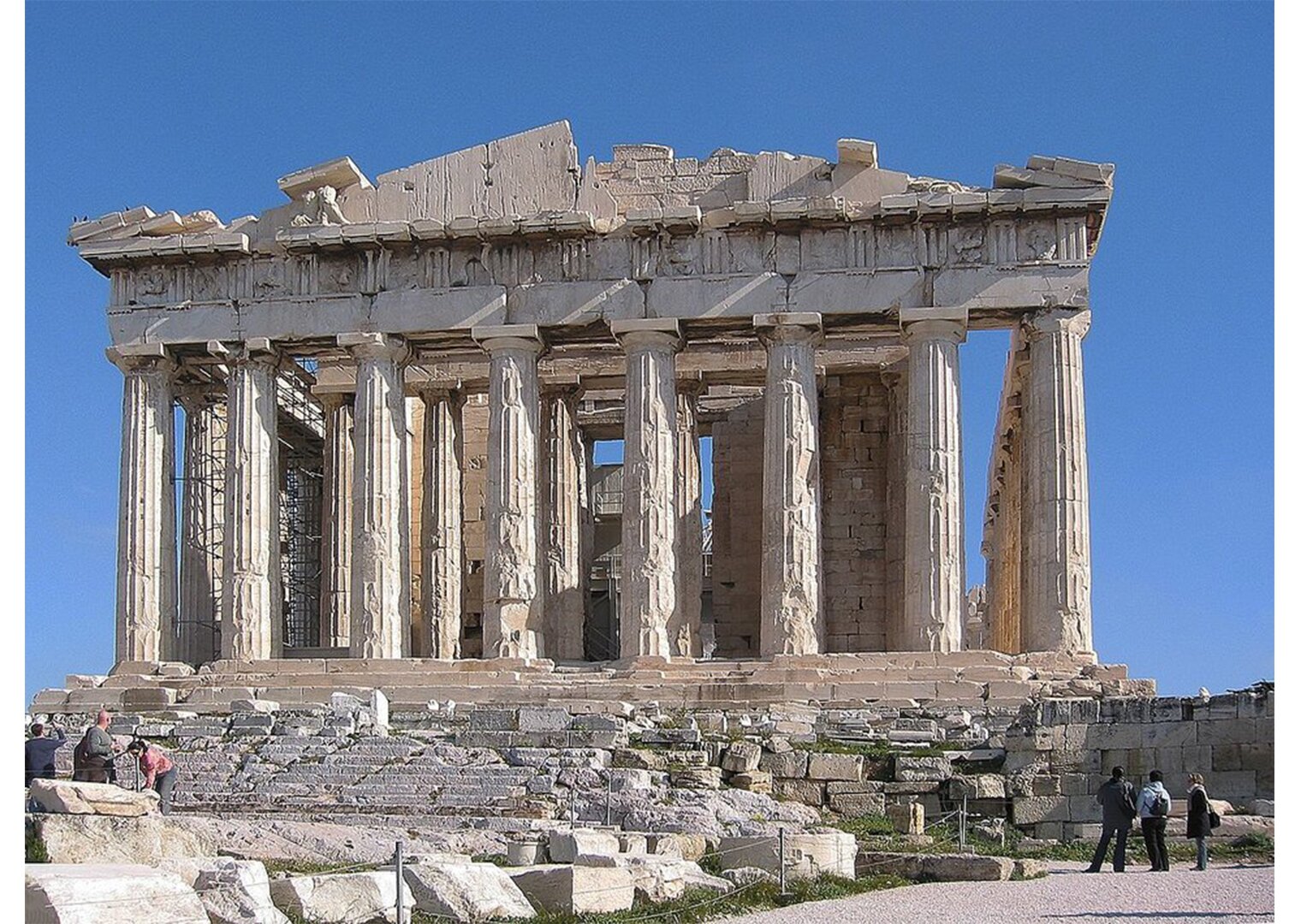 NA zdjęciu pozostałości ateńskiego Partenonu, wykonanego z marmuru. Budowla otoczona kolumnami. 