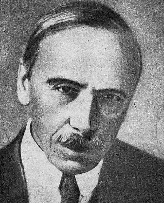 Zdjęcie przedstawia portret dojrzałego mężczyzny. Mężczyzna ma pociągłą twarz, proste włosy zaczesane na prawą stronę. Ma niewielkie wąsy. Jego oczy są osadzone blisko siebie, a nos wydatny. Mężczyzna ubrany jest w garnitur, koszulę i krawat.