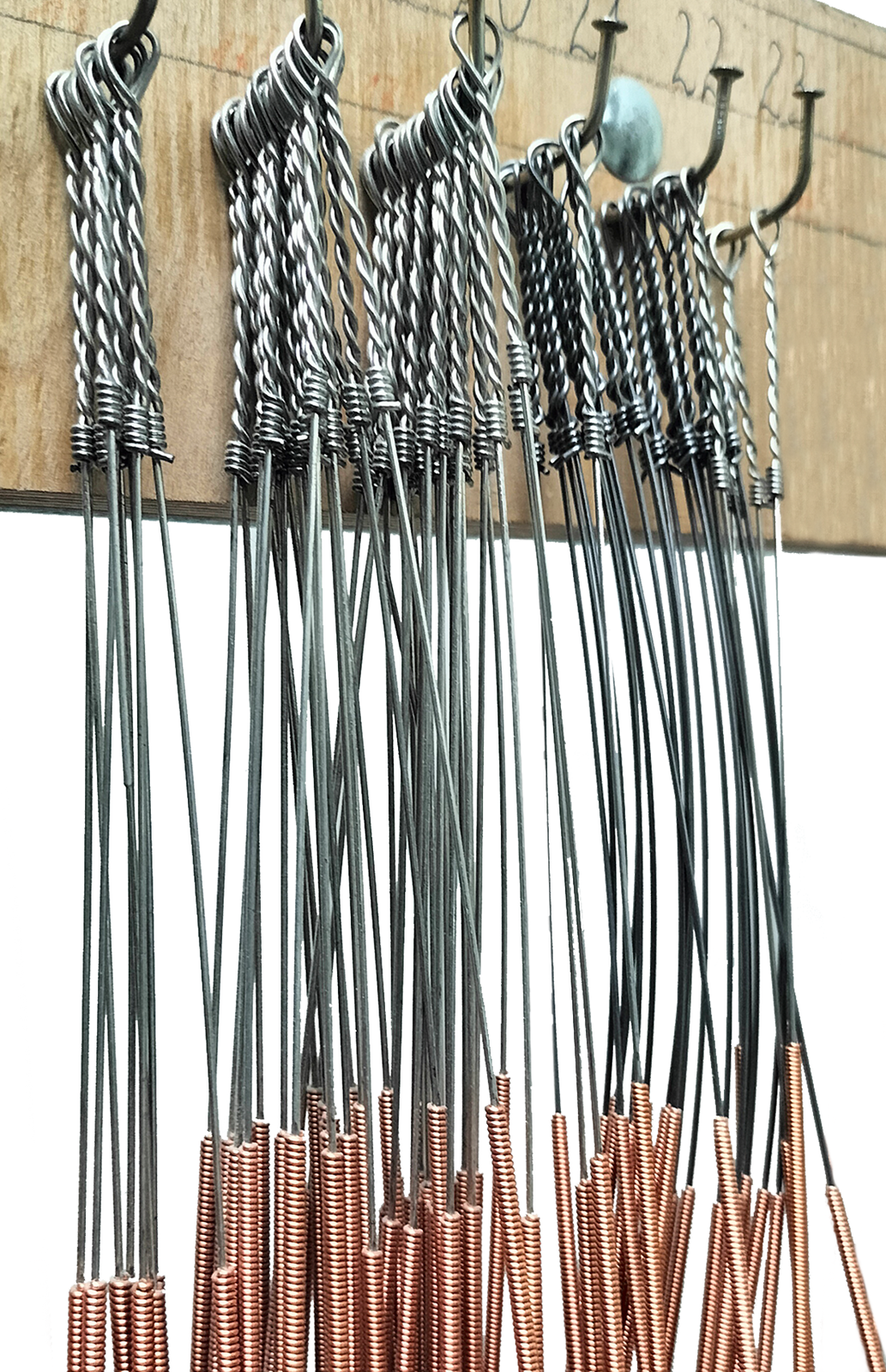 Zdjęcie przedstawia zbliżenie na struny basowe wykonane z drutu miedzianego nawiniętego na rdzeń z drutu stalowego. Widoczne są struny zawieszone pękami na gwoździach wbitych w deskę.