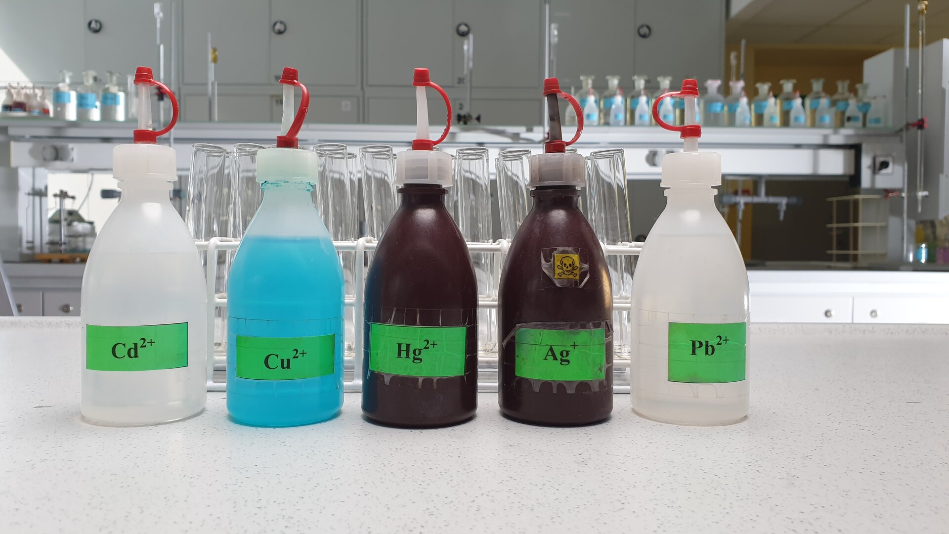 Na stole laboratoryjnym znajdują się buteleczki z roztworami zawierającymi jony kadmu, miedzi, rtęci, srebra i ołowiu.