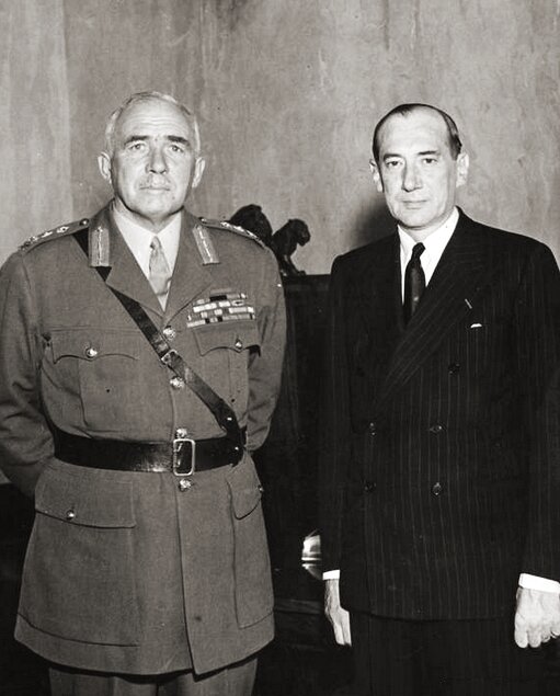 Zdjęcie przedstawia dwóch mężczyzn pozujących do zdjęcia. Mężczyzna po lewej postawny, siwy, ubrany w mundur. Po prawej szpakowaty mężczyzna z zakolami, w garniturze, z białą koszulą i krawatem.