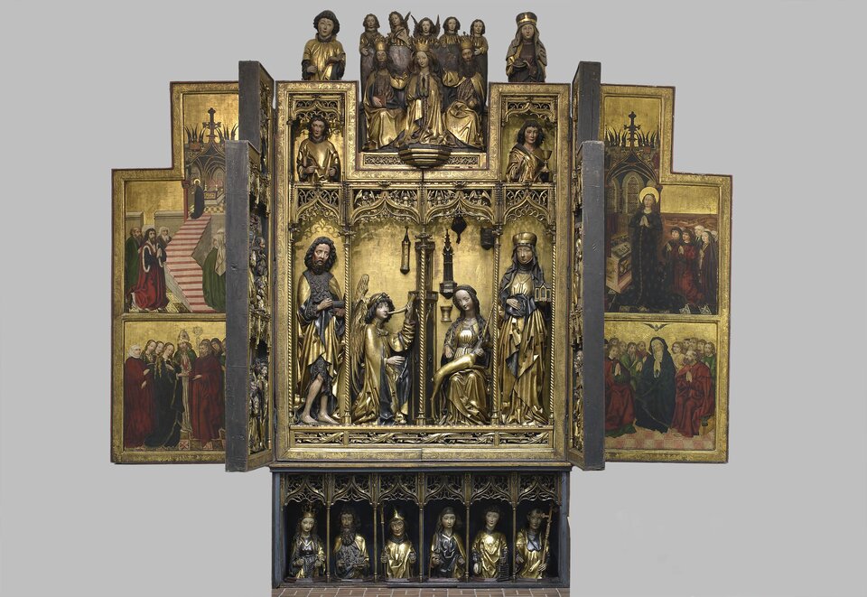 Ilustracja przedstawia poliptyk Zwiastowania z Jednorożcem. Ze środkowej części odchodzą dwa skrzydła z obrazami, natomiast z obu stron głównego przedstawienia znajdują się dwie części poliptyku. Na każdym ze skrzydeł widoczni są święci.