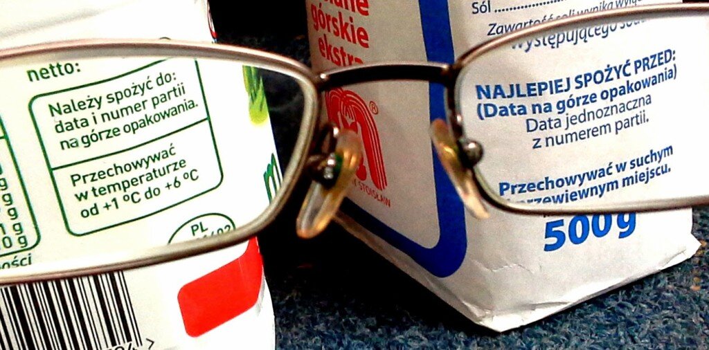 Ilustracja przedstawia zbliżenie na napisy dotyczące dat przydatności na dwóch opakowaniach od mąki lub cukru. Informacje dotyczą tego do kiedy należy spożyć dany produkt, a także w jakiej temperaturze powinno się go przechowywać. Całość jest widoczna przed szkła od okularów.