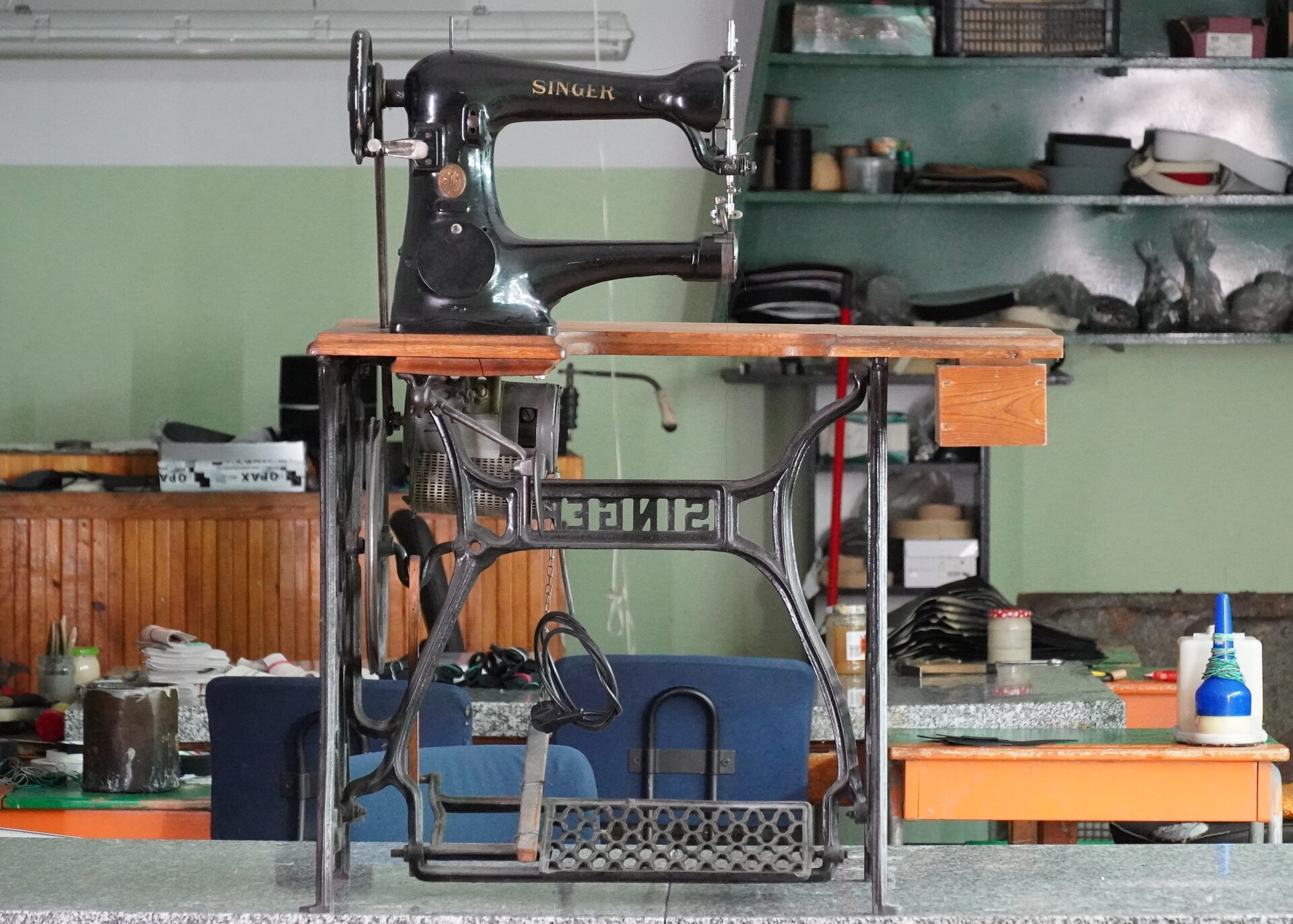 Zdjęcie przedstawia czarną maszynę leworamienną do szycia starego typu Singer stojącą na drewnianym stoliku z żelazną podstawą. Z boku maszyny jest duże pokrętło. Nagranie tożsame z treścią.