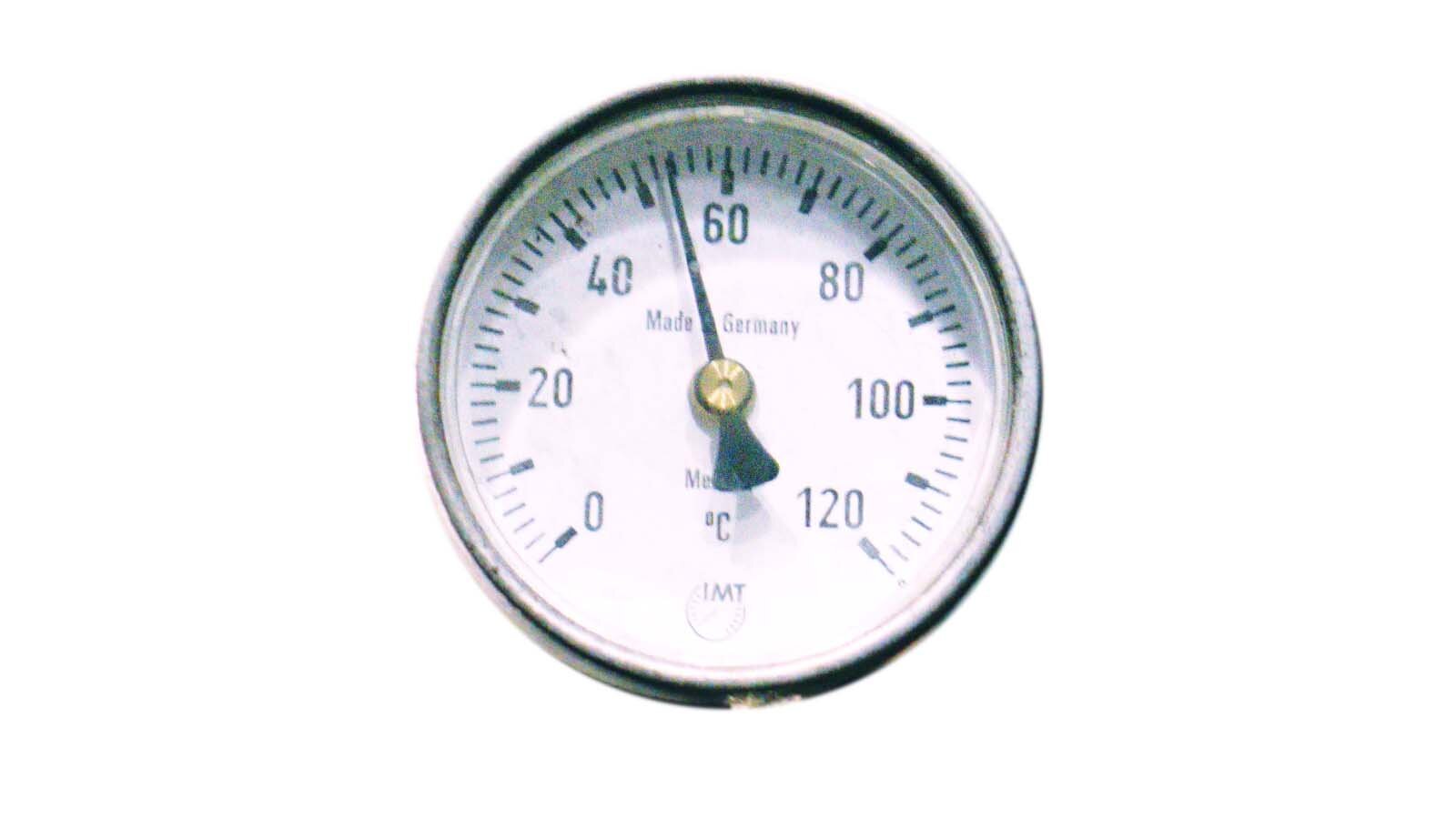  Ilustracja przedstawia manometr. Urządzenie kształtem przypominające zegar. Wewnątrz za szklaną szybką znajduje się czarna wskazówka za nią skala. Opis skali zaczyna się od zera ukazując kolejne wartości co dwadzieścia, aż do stu dwudziestu. Skala określa stopnie Celsjusza. Wskazówka ukazuje wartość pięćdziesiąt cztery stopnie Celsjusza.