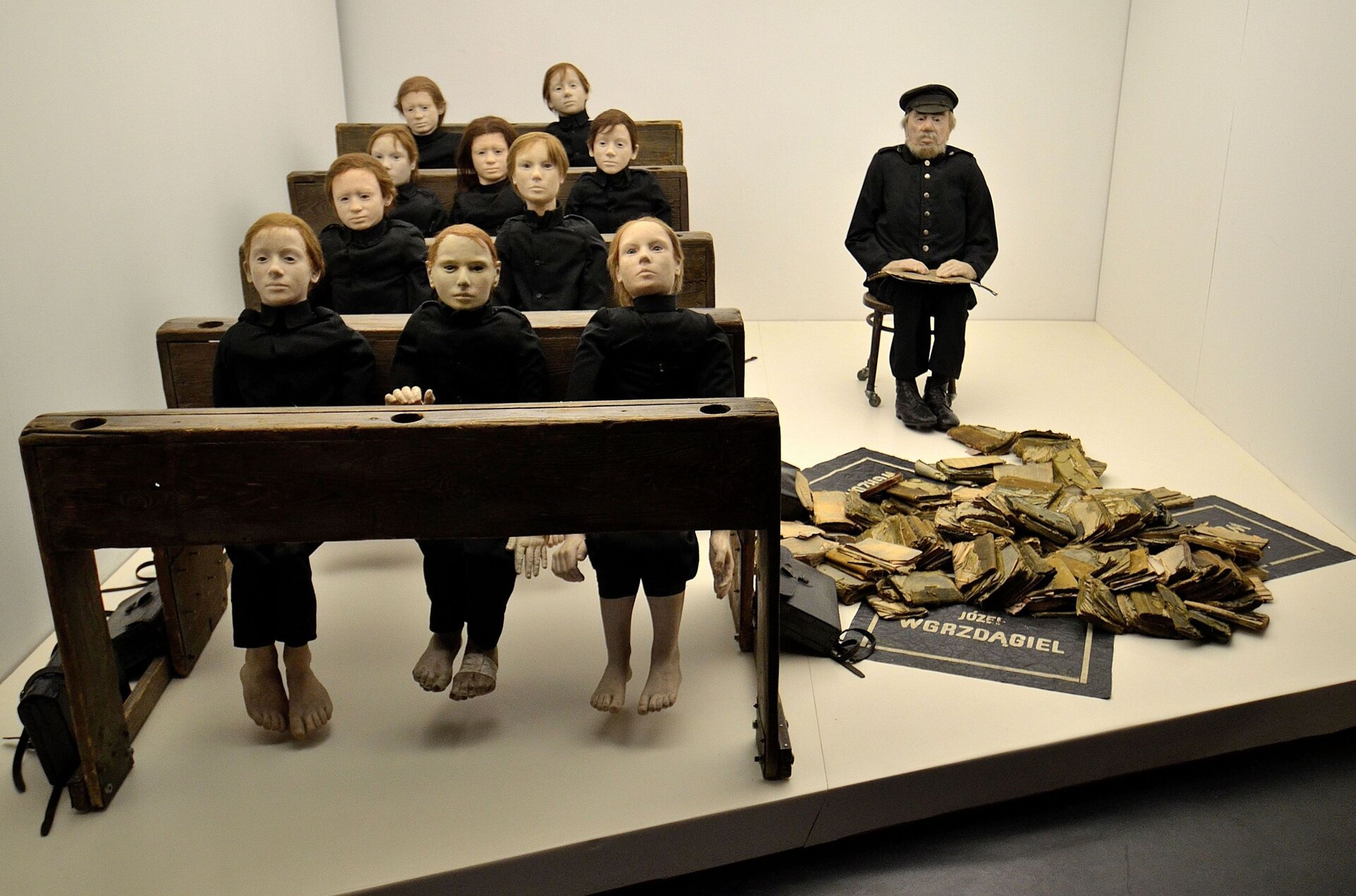Instalacja artystyczna przedstawia wnętrze klasy szkolnej – pięć ławek, przy których siedzi 10 uczniów. Nauczyciel siedzi na krześle umieszczonym z tyłu klasy, przy ostatnich rzędach ławek. Ławki wykonane zostały z ciemnego drewna, zaś uczniowie to lalki. Ubrane są na czarno, mają jasne twarze oraz włosy w różnych odcieniach rudości. Nie mają na sobie butów, widoczne są ich stopy, niesięgające podłogi. Patrzą przed siebie. Nauczyciel również jest ubrany na czarno, jest mężczyzną w podeszłym wieku o siwej brodzie oraz z czapką z daszkiem na głowie. Na kolanach trzyma otwartą książkę. Ściany są kremowe, a na kremowej podłodze z przodu klasy widać stos kartek przypominających pożółkłe książki oraz plakaty – czarne tło, złota ramka oraz złoty napis „Józef Wgrzdągiel”.