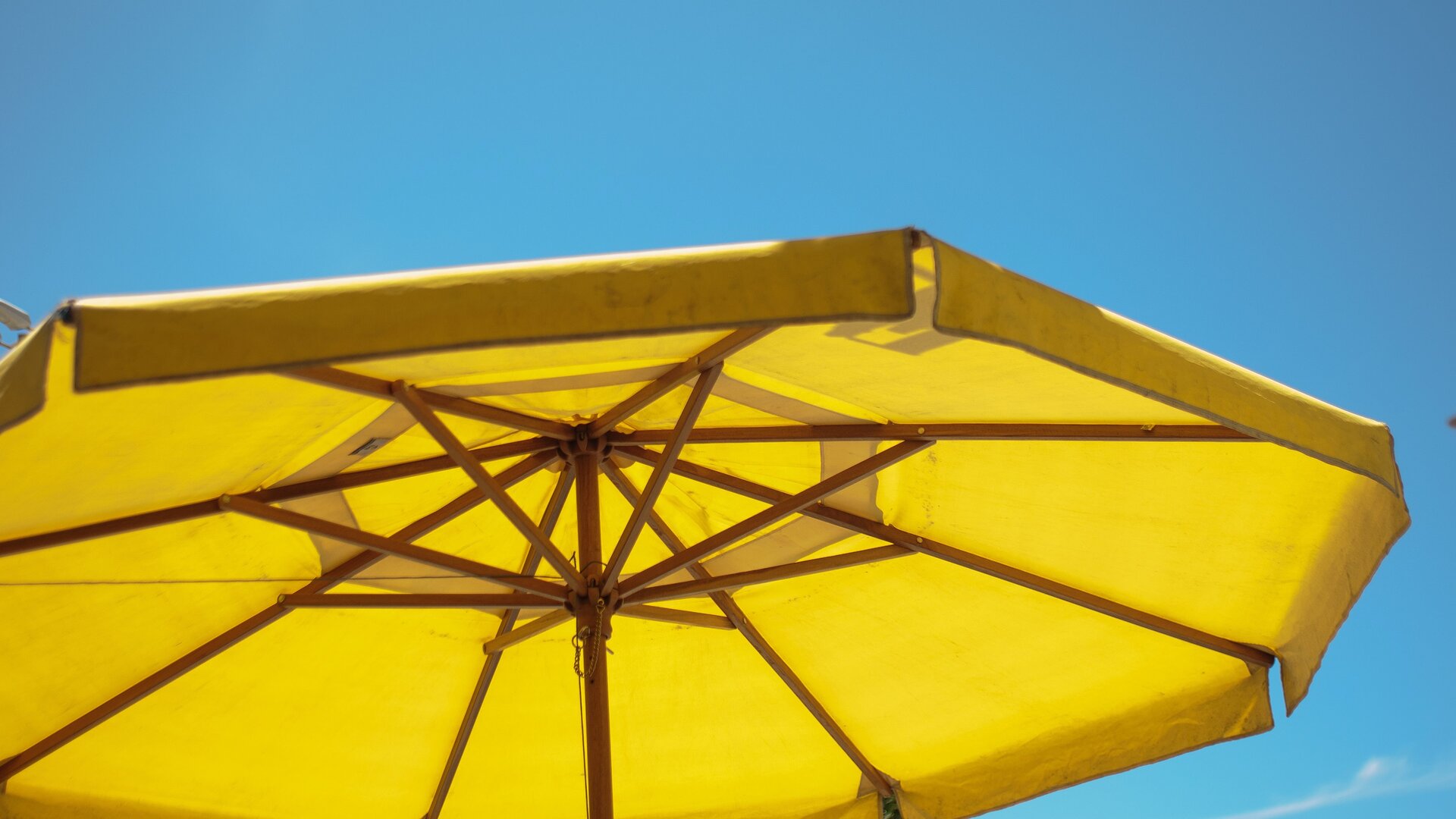 Zdjęcie przedstawia żółty parasol przeciwsłoneczny na tle błękitnego, bezchmurnego nieba.