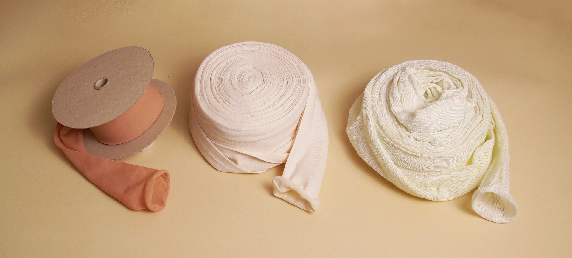 Zdjęcie przedstawia wąż ortopedyczny. Na blacie znajdują się trzy zwinięte węże ortopedyczne. Pierwszy od lewej nawinięty jest na szpulę i ma pomarańczowo‑brązowy kolor. Drugi i trzeci są zwinięte i są koloru białego.