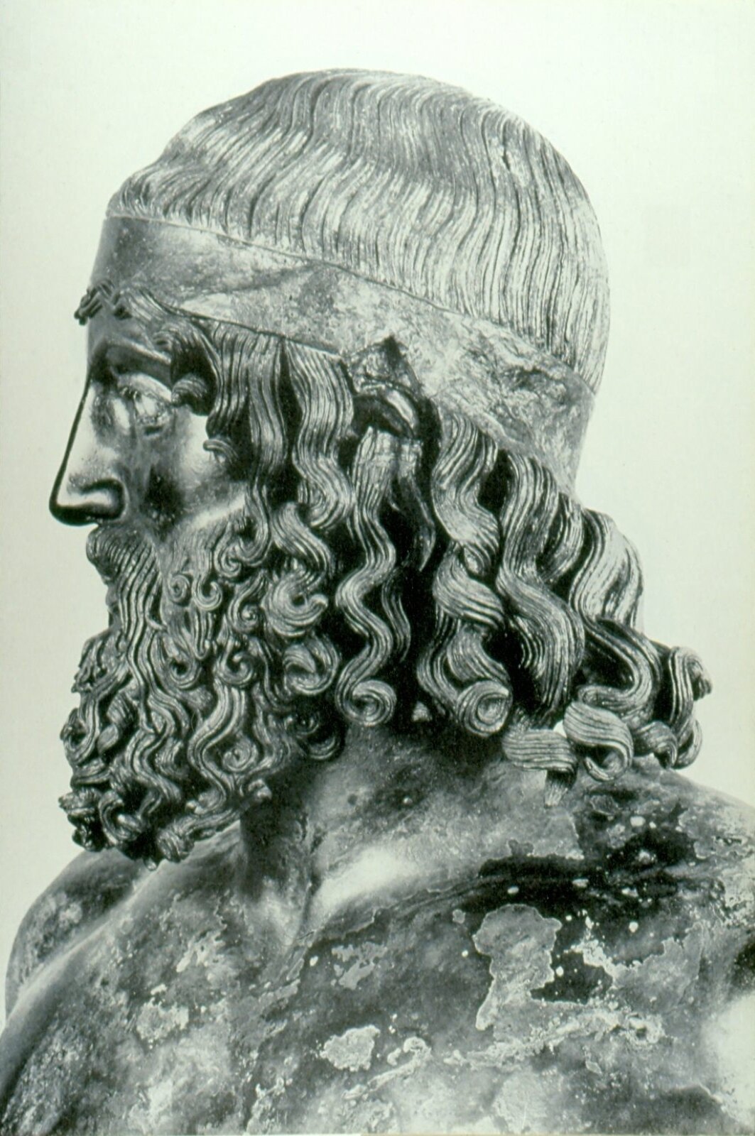 Ilustracja przedstawia popiersie mężczyzny w podeszłym wieku o długich kręconych włosach i bujnym zaroście. Ma on duże, szeroko otwarte oczy. Na czarnym kamieniu rzeźby widoczne są uszkodzenia i odbarwienia.